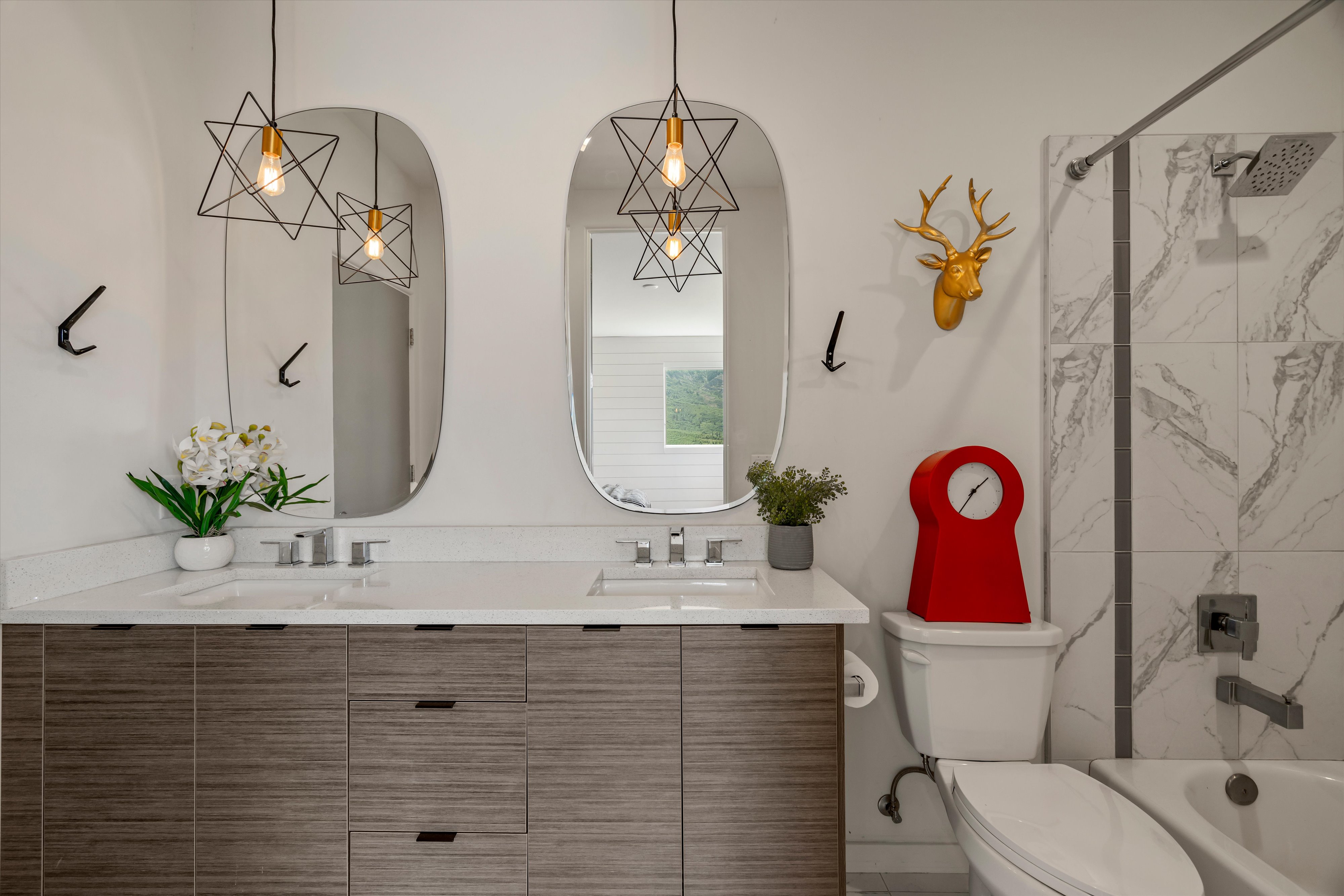 Dual vanity with integrated sinks and wood-finish cabinetry, illuminated by two geometric pendant lights