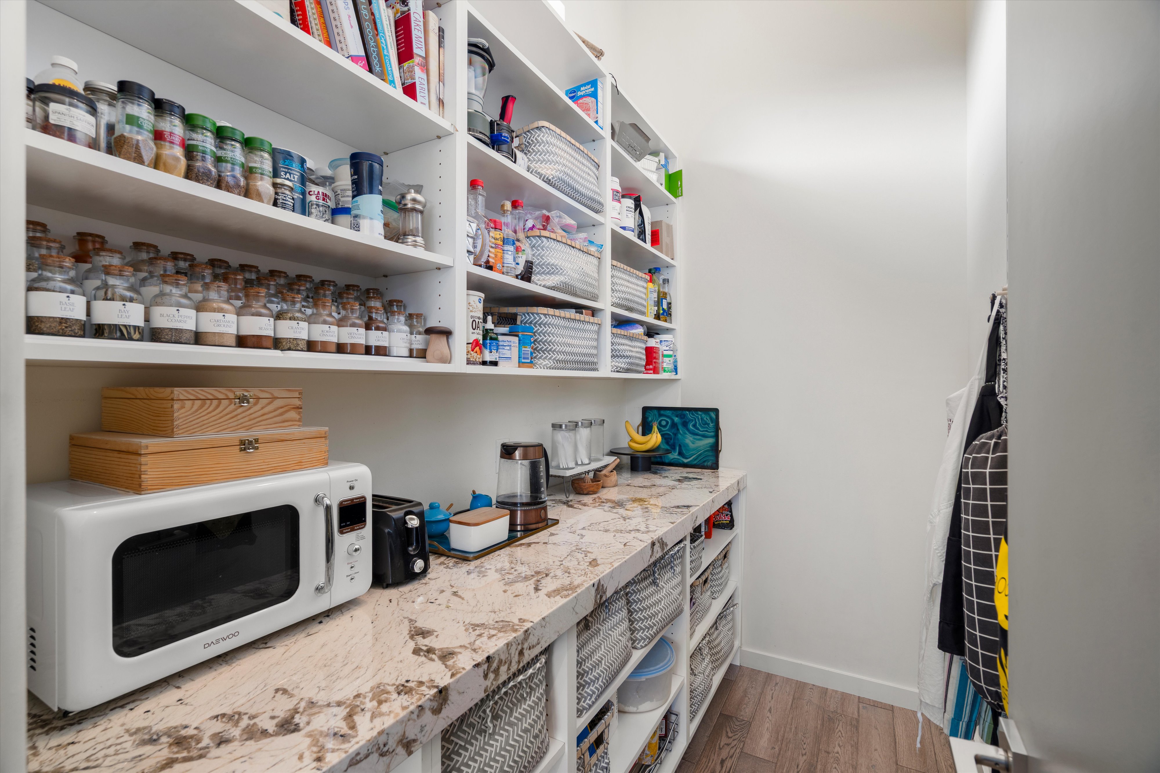 Walk-in pantry featuring extensive built-in shelving, a spacious countertop, wood-finish flooring, and white cabinetry