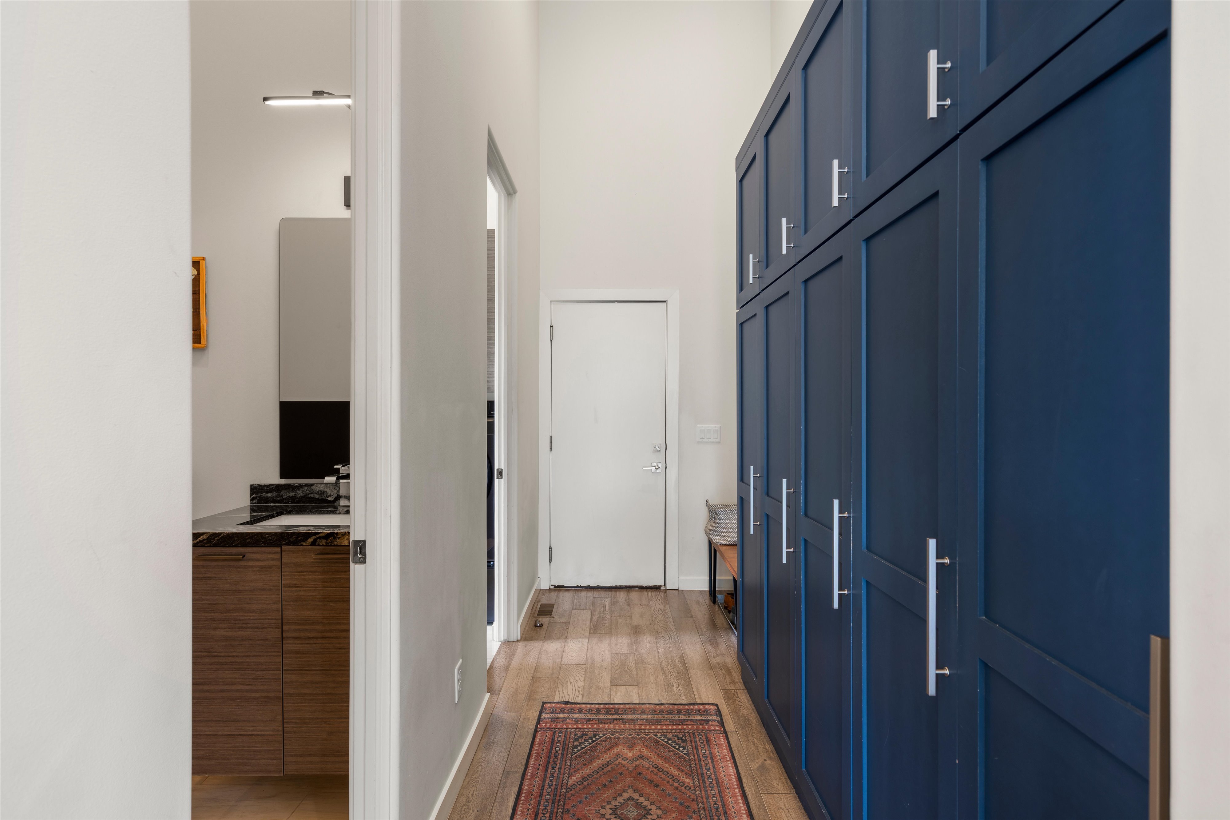 Hallway featuring floor-to-ceiling blue cabinetry with silver hardware, wood-finish flooring, and a high ceiling