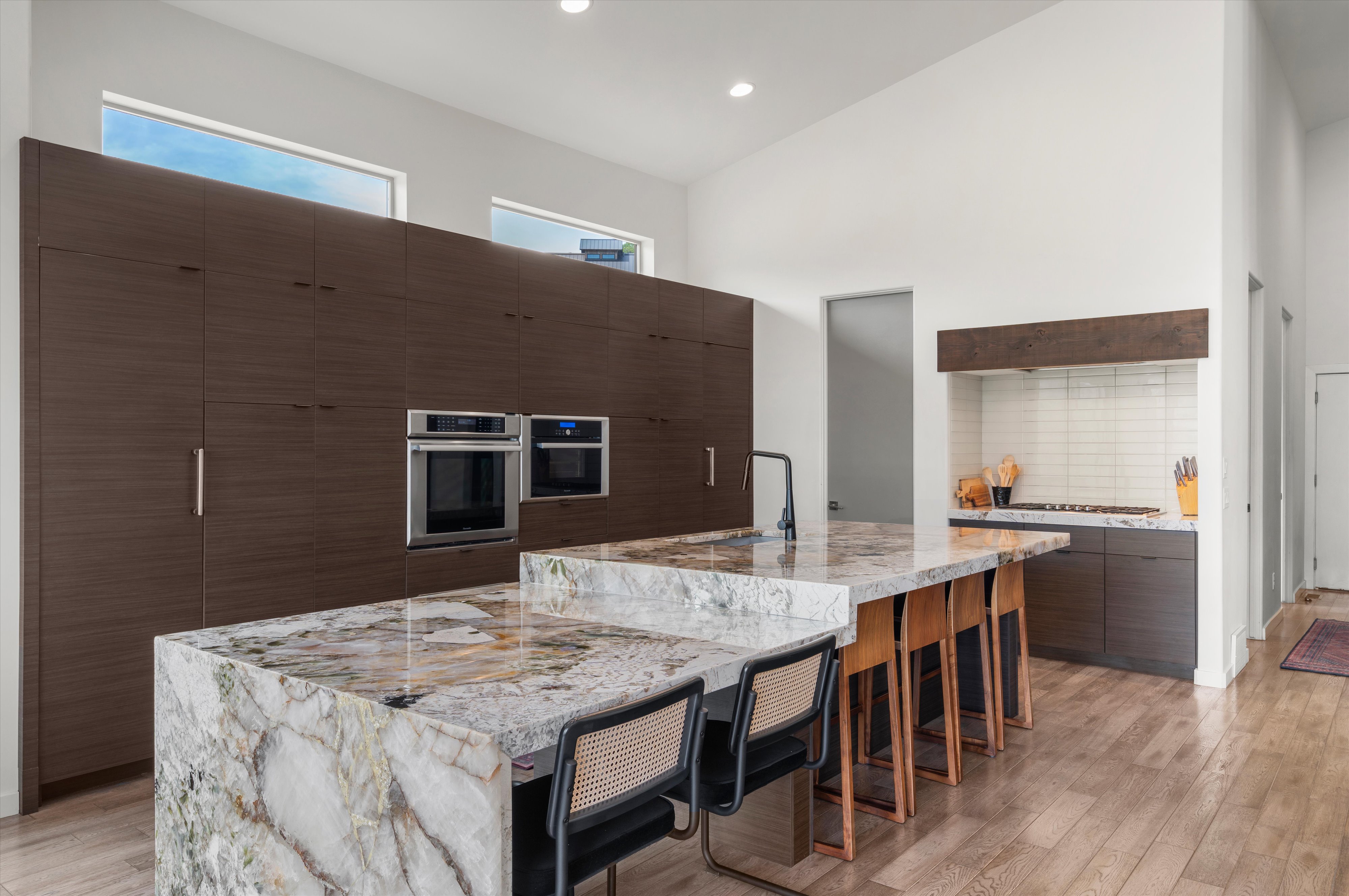 Kitchen featuring extensive dark wood-finish cabinetry, integrated ovens, and two multi-level islands with stone countertops