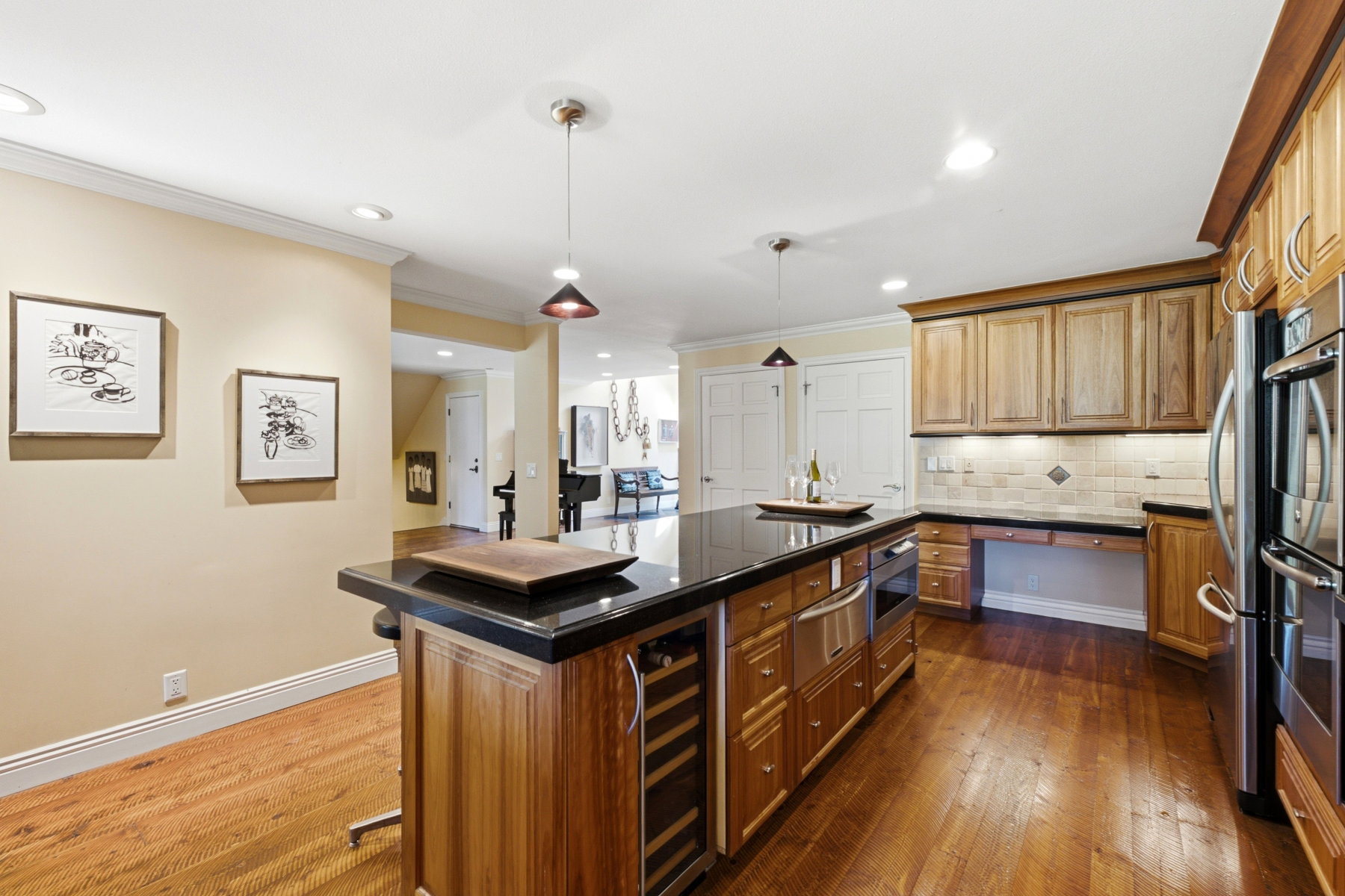 Gourmet kitchen featuring a substantial island with a dark countertop and integrated wine refrigerator, stainless steel appliances, wood-finish flooring, and natural wood cabinetry with under-cabinet lighting