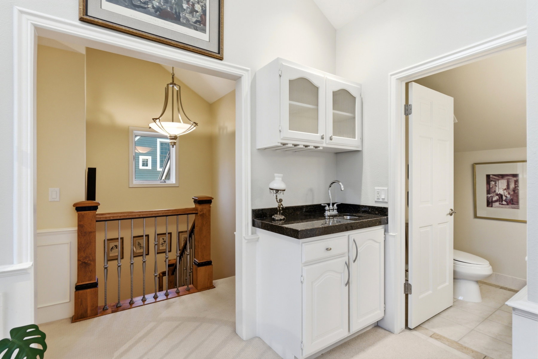 Hallway wet bar featuring white cabinetry, a dark countertop, and a stainless steel sink