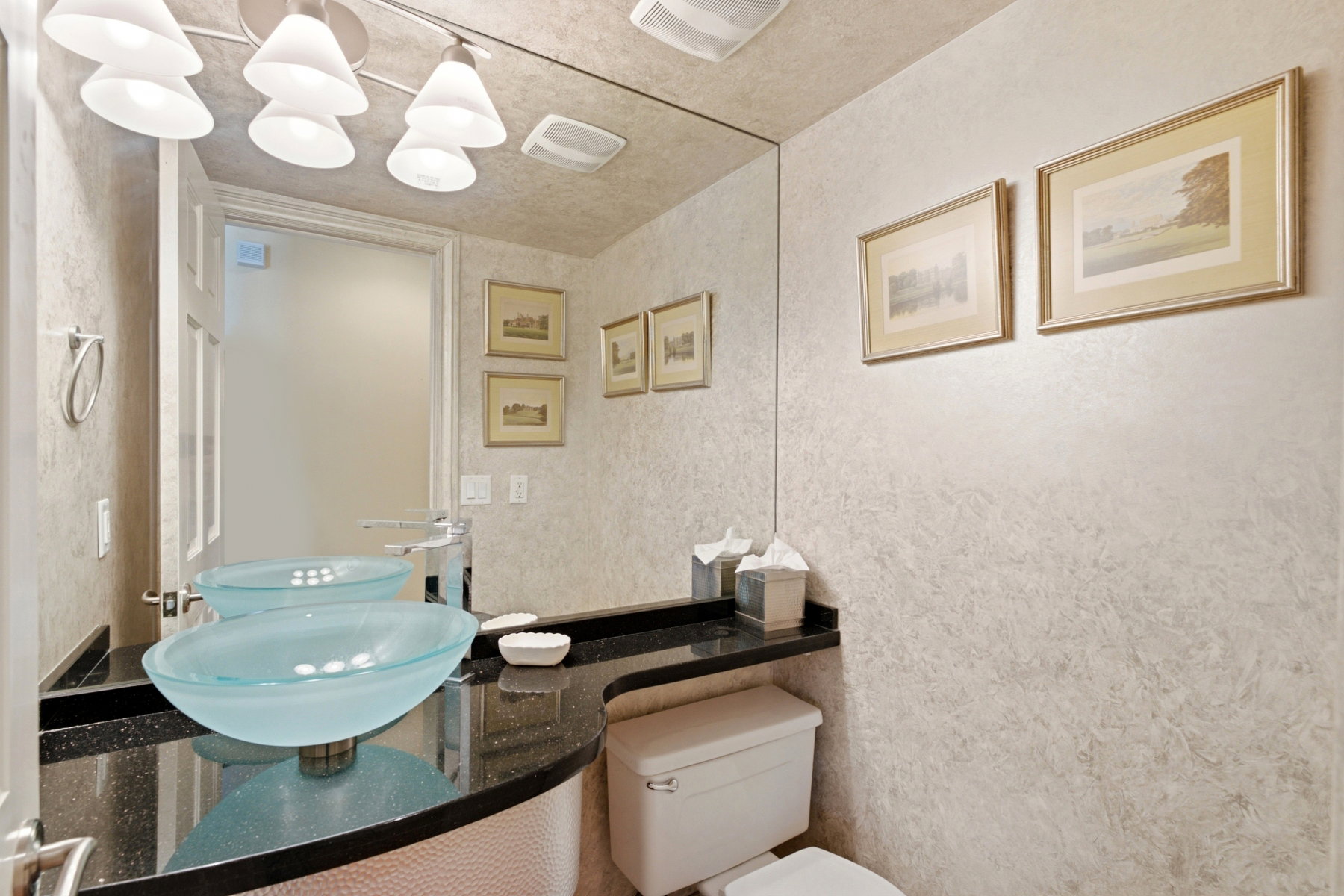 Double vessel sinks with frosted glass bowls set into a dark countertop, full-height mirror, and textured wall finish