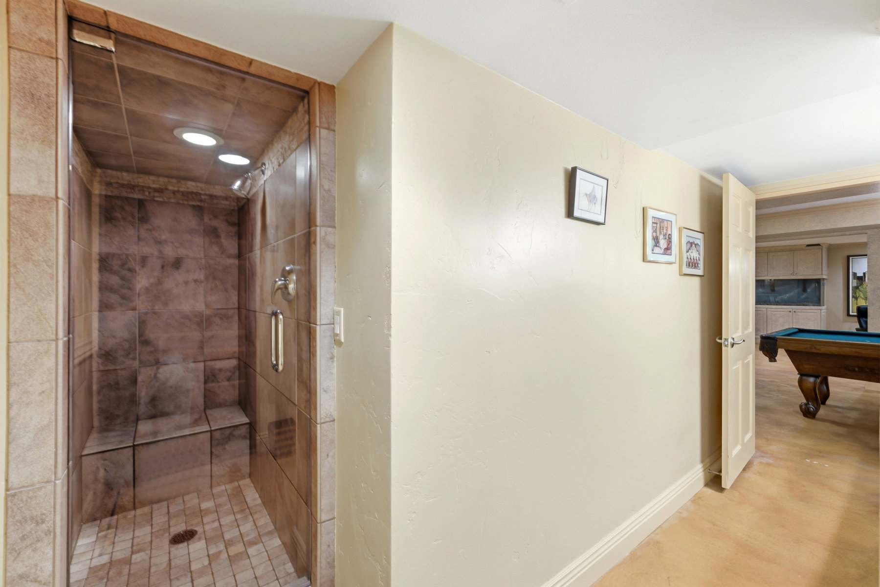 Glass-enclosed shower with tiled walls and flooring, featuring a built-in bench, recessed lighting, and a chrome shower fixture