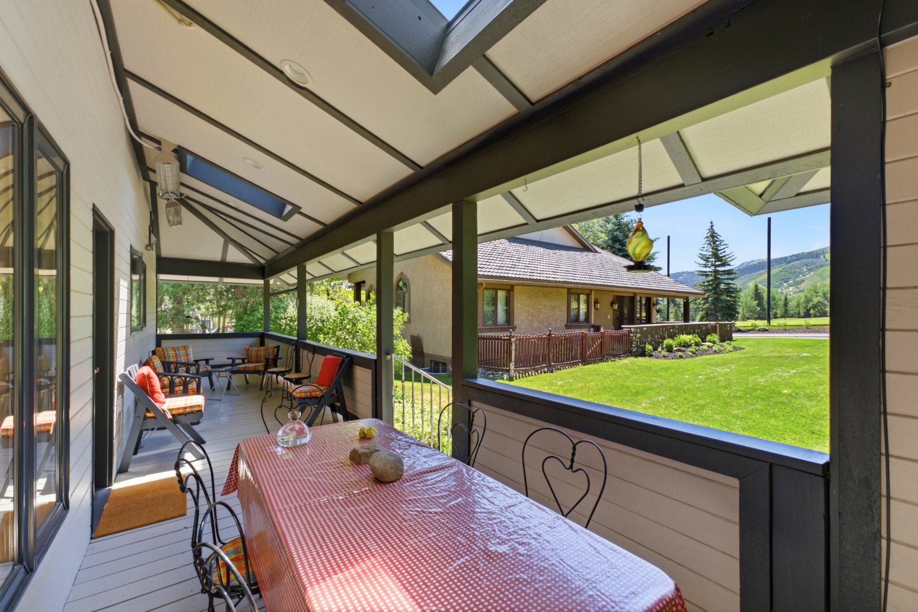 Covered outdoor patio featuring a vaulted ceiling with skylights, light-toned wood-finish flooring, and black railing