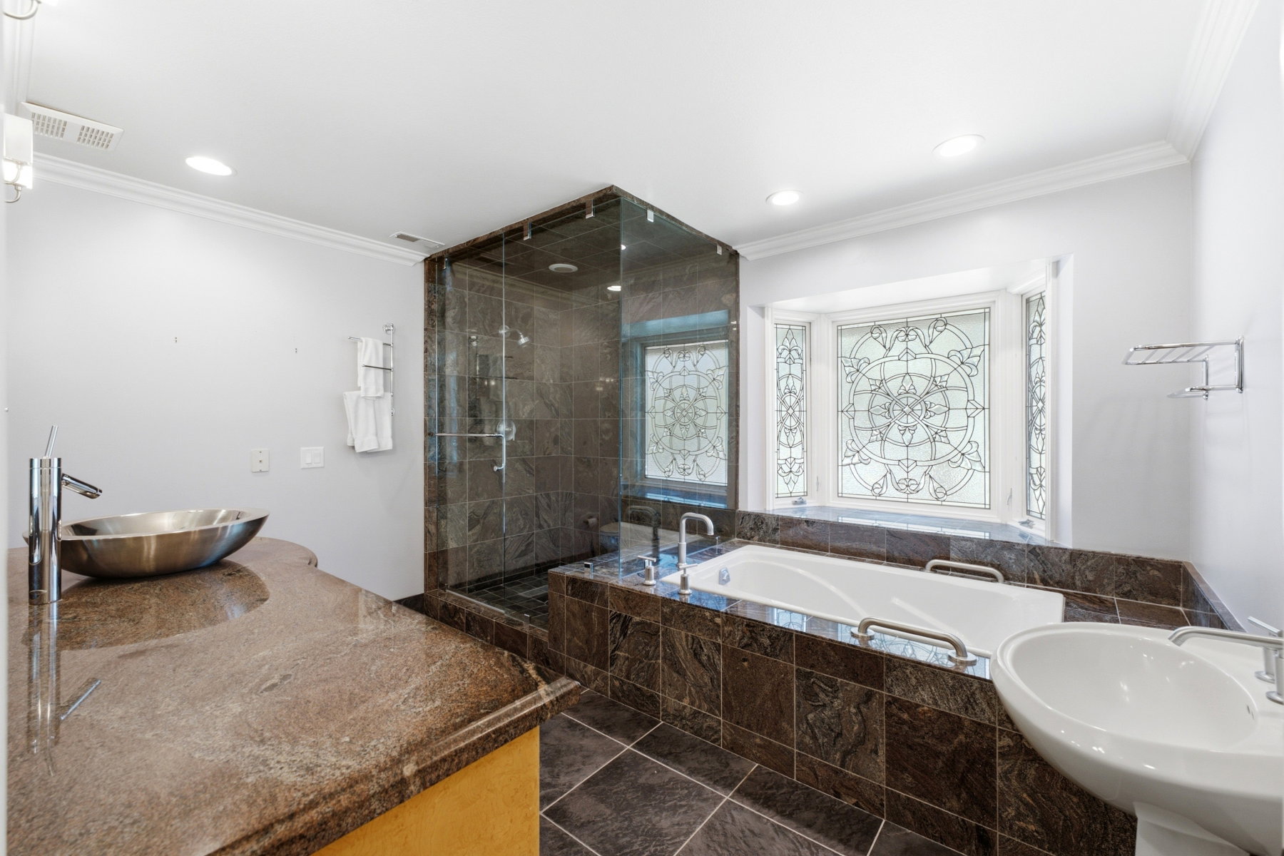 Bathroom featuring a built-in tub, separate glass-enclosed shower, stone tile flooring, a vessel sink, and a stained glass window