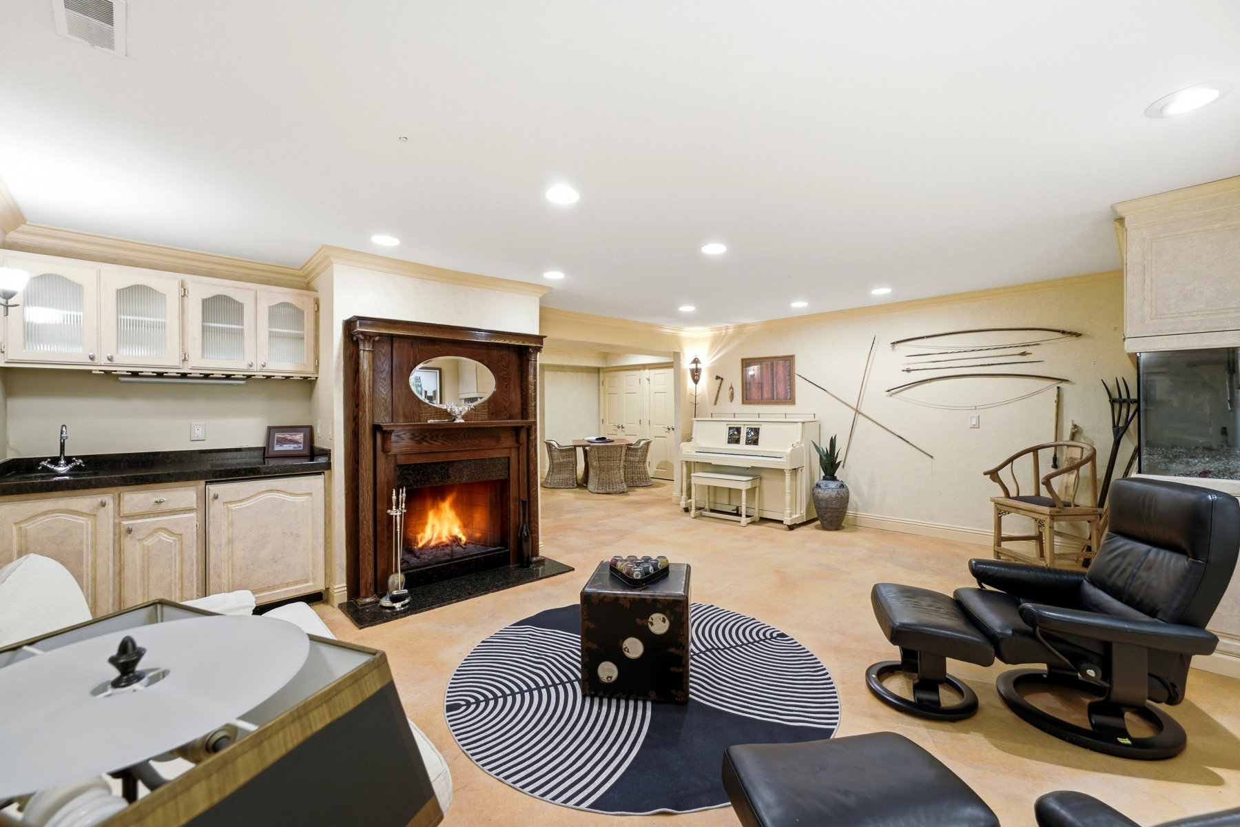 Expansive lower-level space featuring a dark wood-surround fireplace with a black stone hearth, recessed lighting, and light-toned flooring