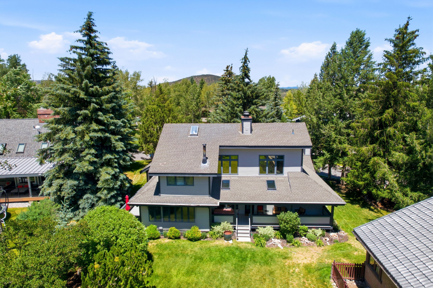 Contemporary multi-level residence featuring a gray exterior, a dark shingle roof, and multiple skylights