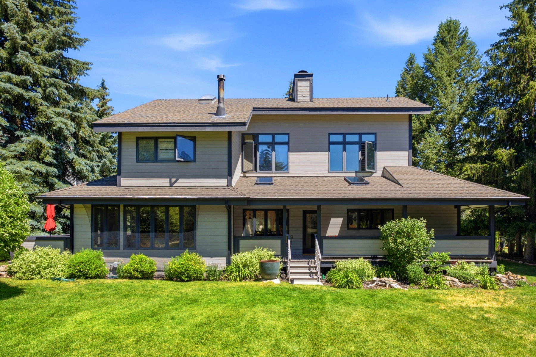 Contemporary two-story residence featuring a broad covered porch, multiple skylights, and a prominent chimney