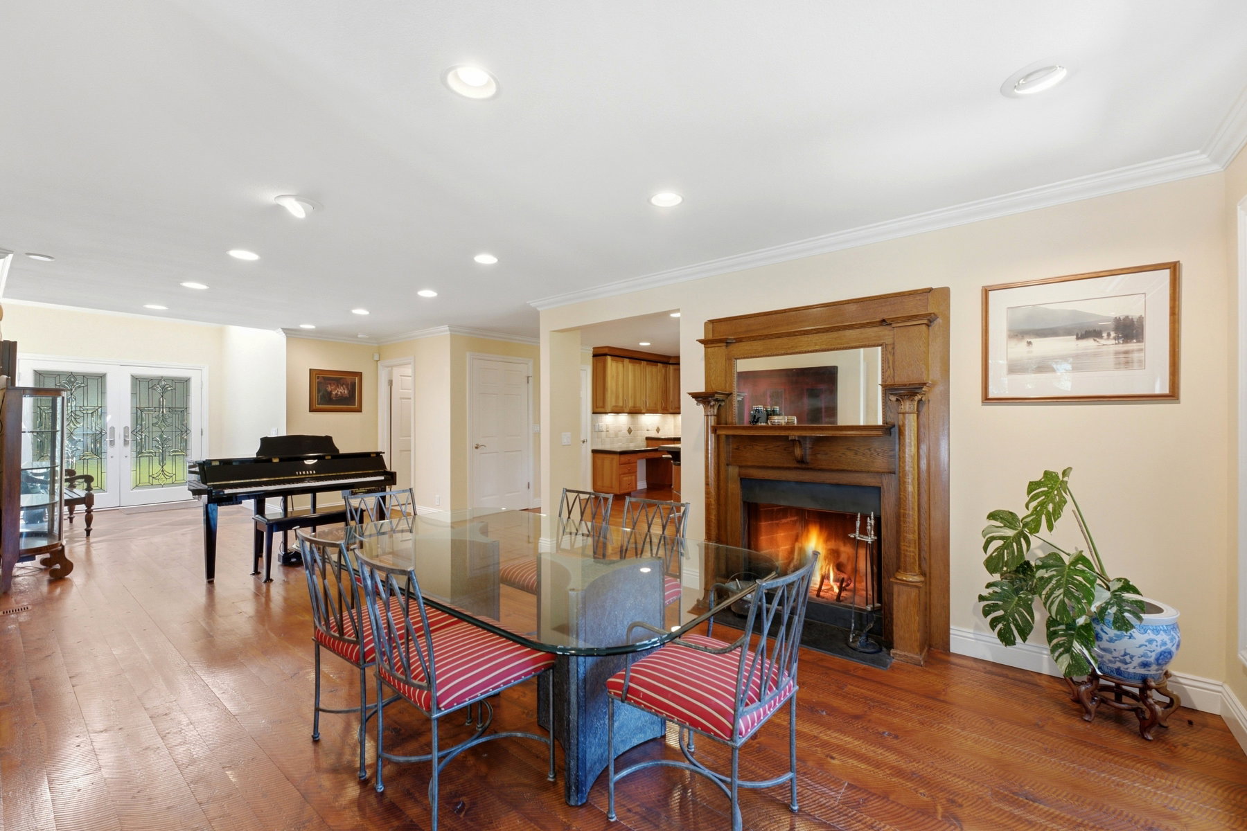 Spacious interior featuring wood-finish flooring throughout, a detailed wood mantel surrounding a fireplace, recessed ceiling lighting, and French doors leading to exterior