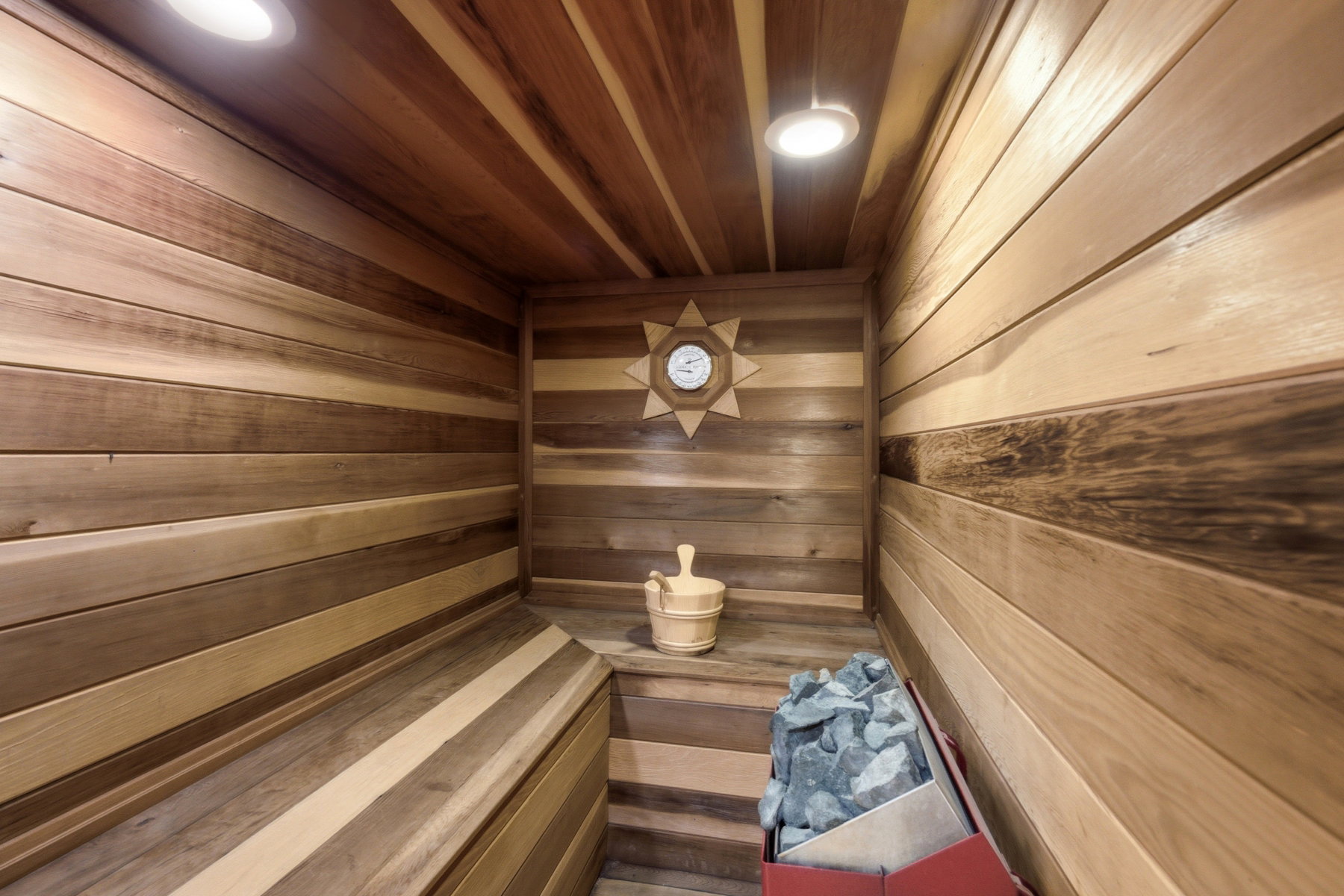 Custom sauna featuring wood plank walls and ceiling, built-in wooden bench seating, and recessed lighting