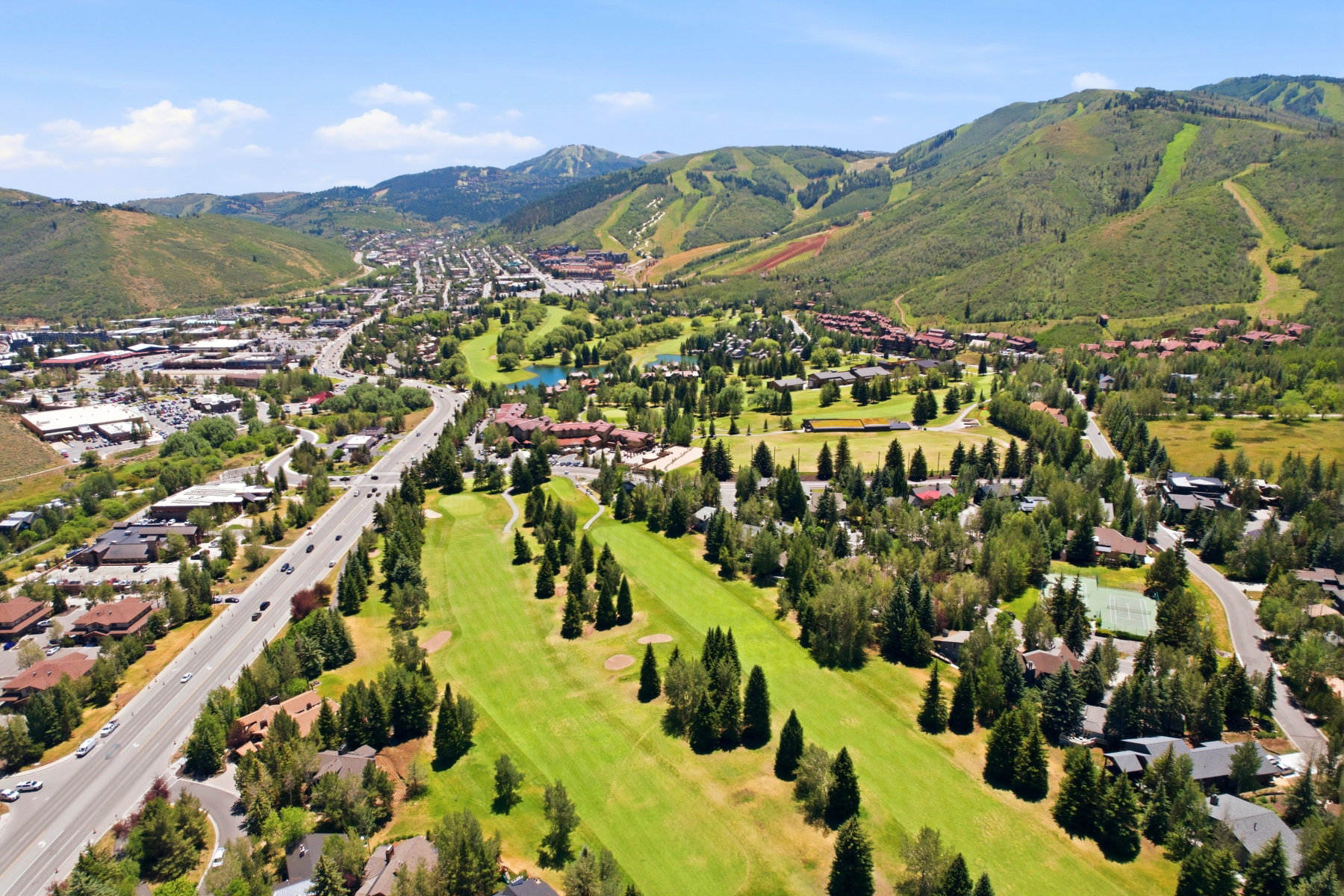 Expansive aerial landscape featuring a golf course, surrounding residential properties, commercial structures, and a multi-lane roadway