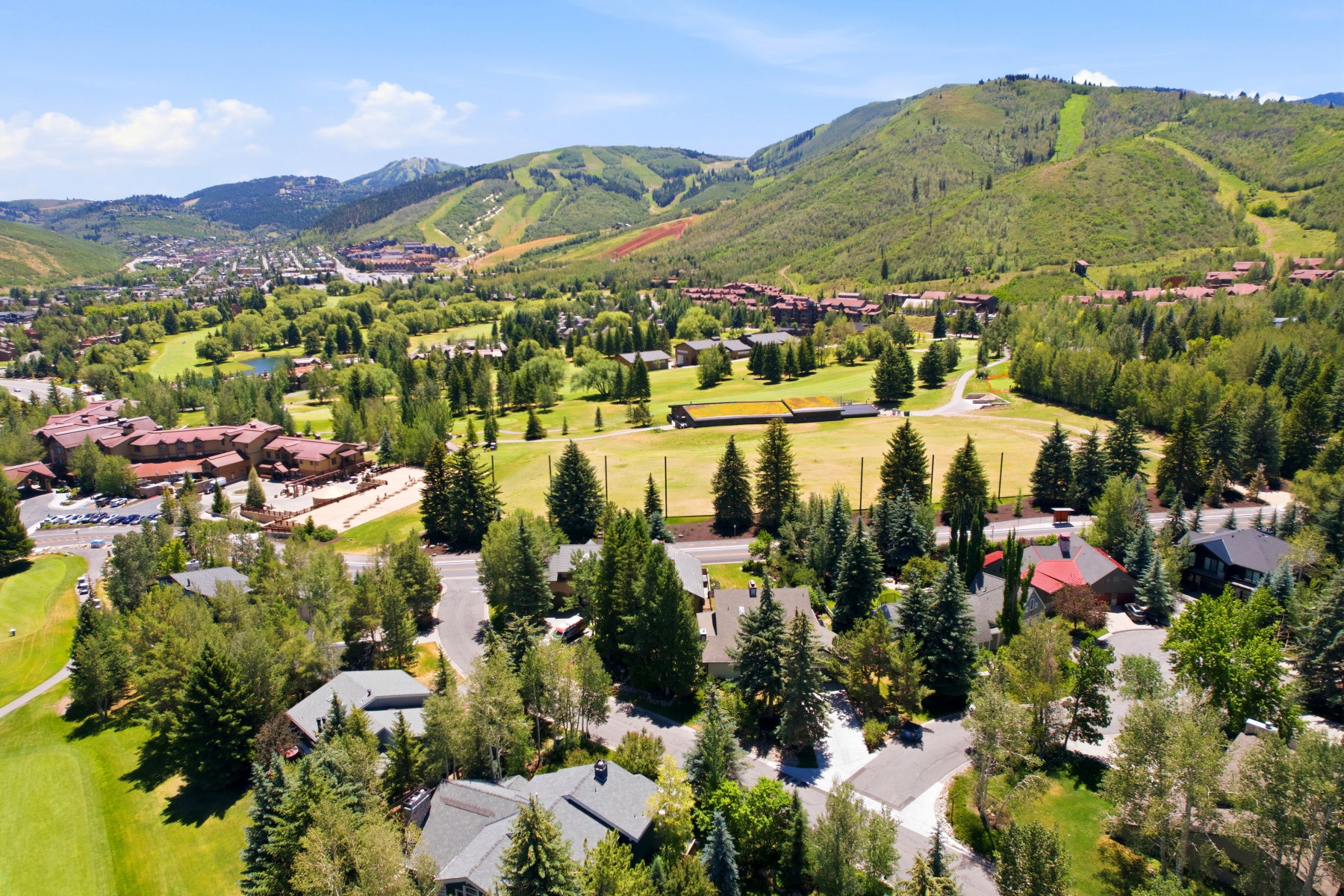 Expansive natural landscape featuring lush green golf course fairways, scattered mature trees, and mountainous terrain in the background