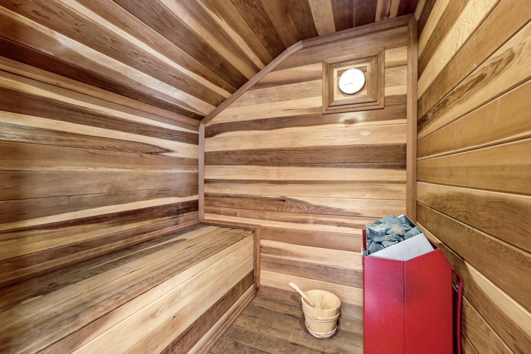 Dedicated sauna room featuring natural wood-finish paneling, an integrated wood bench, and a mounted thermometer