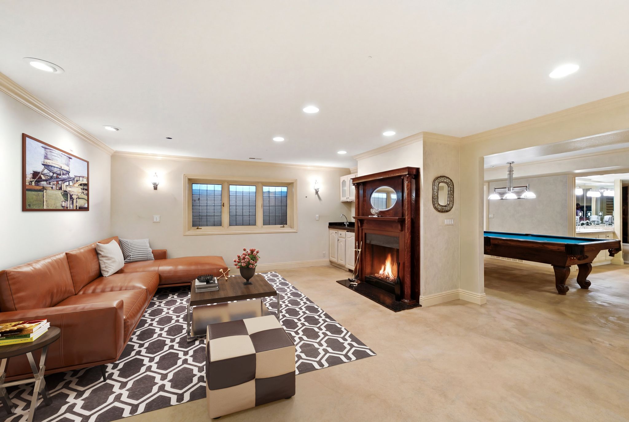 STAGED PHOTO-Finished lower level featuring a fireplace with a wood surround, a wet bar with white cabinetry, and recessed lighting - staged family room lower level