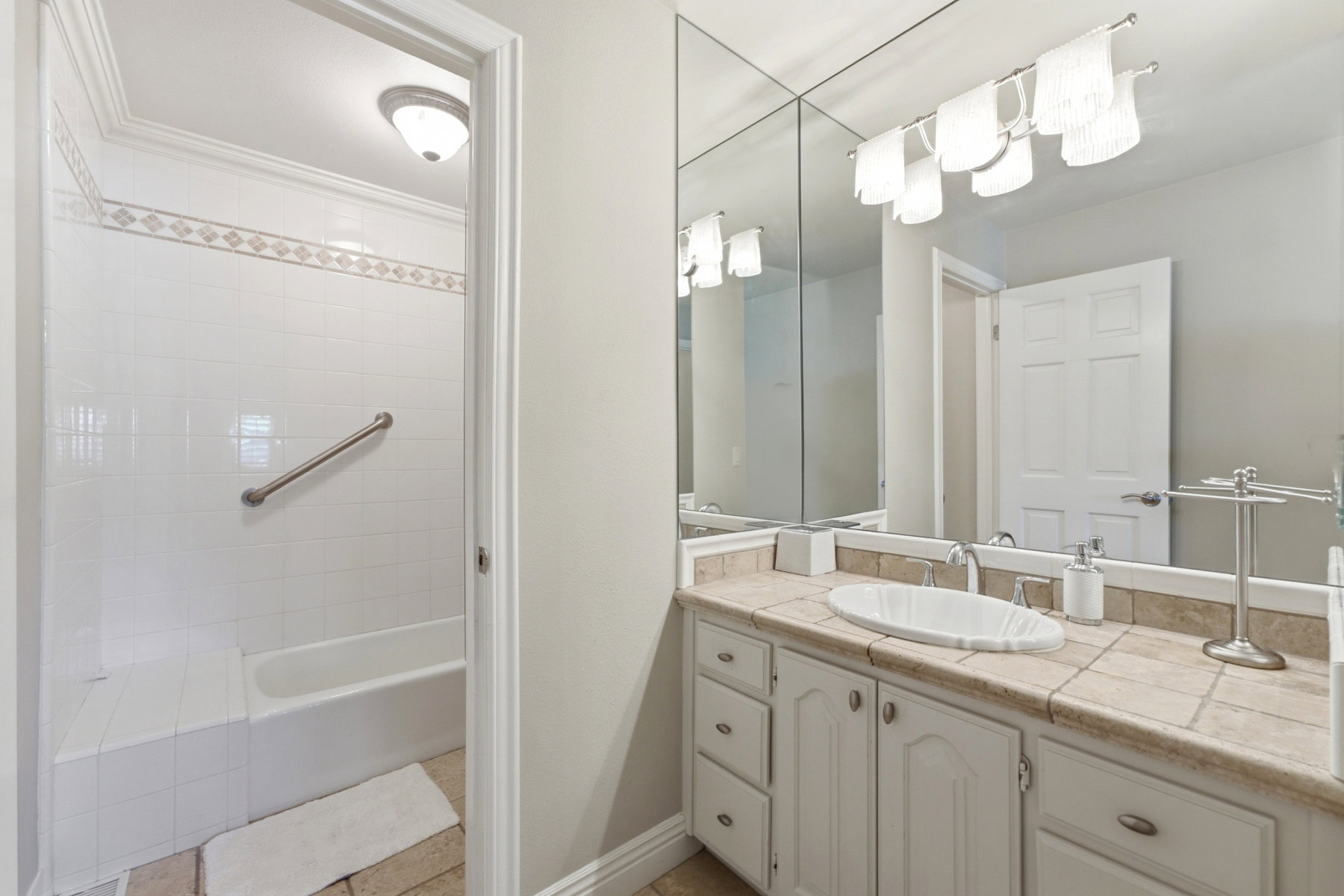 Bathroom featuring a white tile tub/shower combination with decorative accent tile and a built-in bench