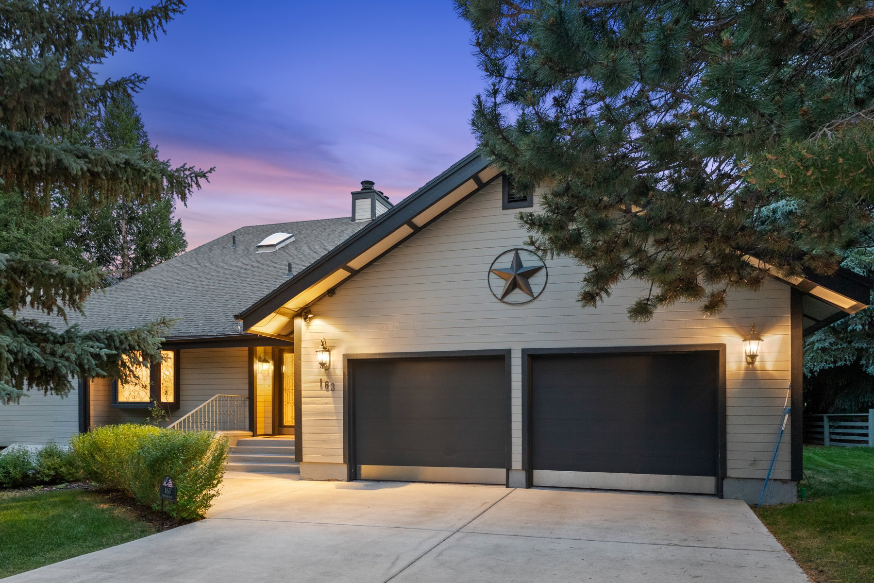 Exterior featuring light-toned siding with dark trim, a two-car garage, and multiple outdoor wall sconces