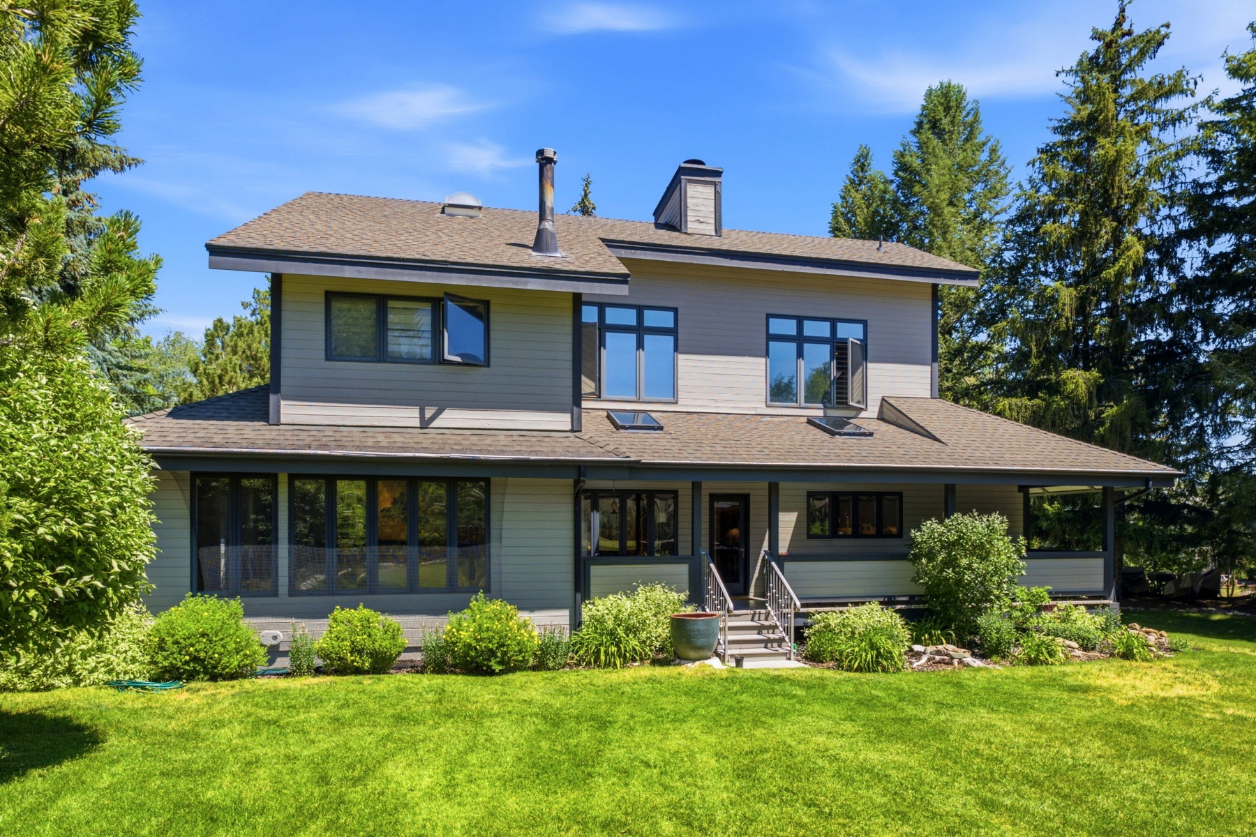 Contemporary exterior design featuring multiple rooflines, a covered front porch, an abundance of windows, and mature perimeter trees