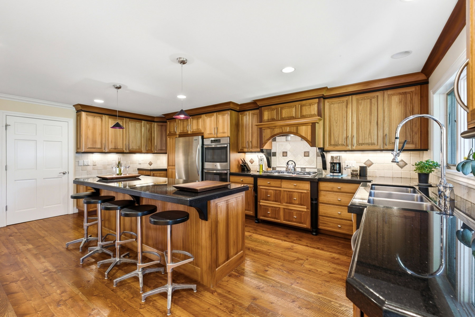 Kitchen featuring wood-finish cabinetry, dark countertops, a large island with seating, a built-in stainless steel double oven, and recessed lighting