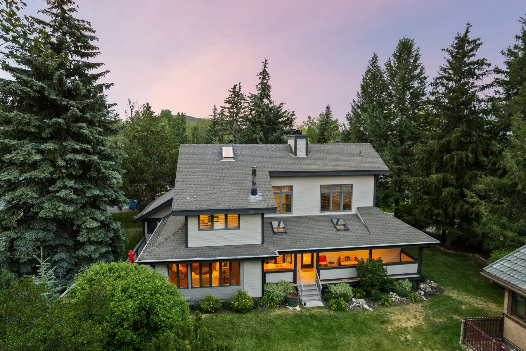 Contemporary multi-level residence featuring a covered porch, abundant natural light, a stone chimney, and a landscaped yard