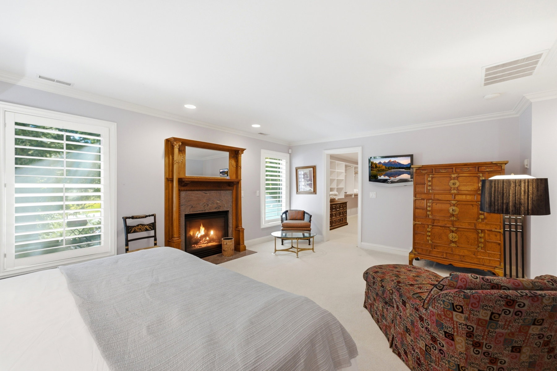 Carpeted room featuring a fireplace with a wood mantle and stone surround, two large windows with plantation shutters, recessed lighting, and crown molding