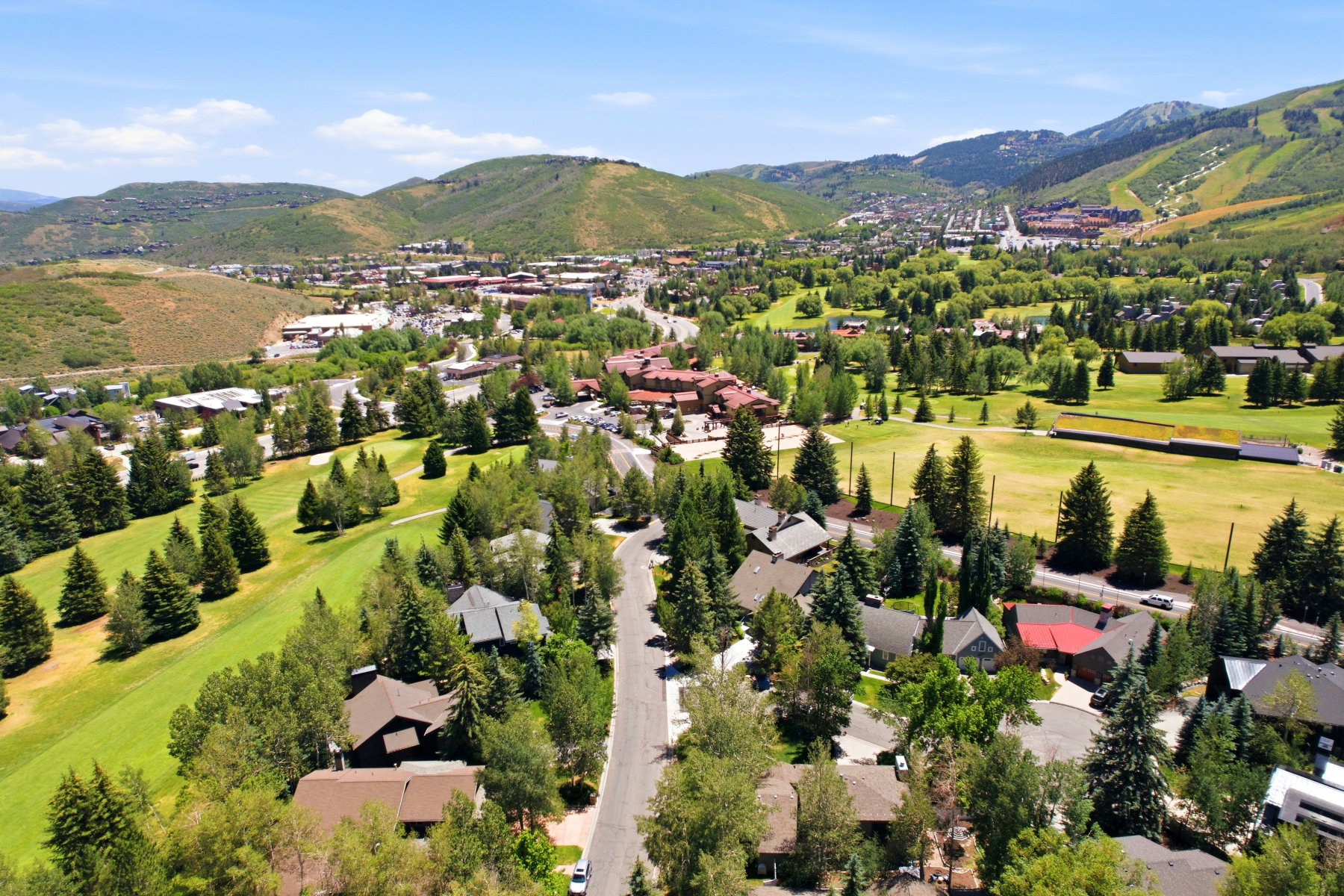 Aerial landscape featuring a vibrant green golf course, a mountainous backdrop, and residential properties with varied rooflines