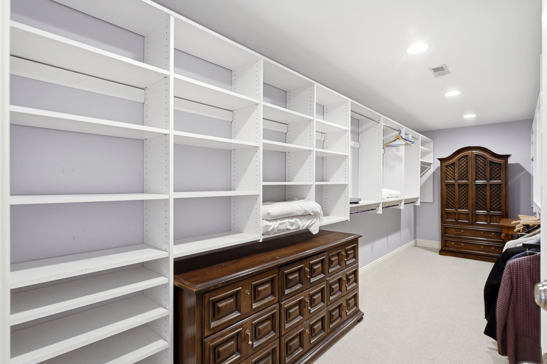 Spacious closet featuring extensive white built-in shelving, recessed lighting, and carpet flooring