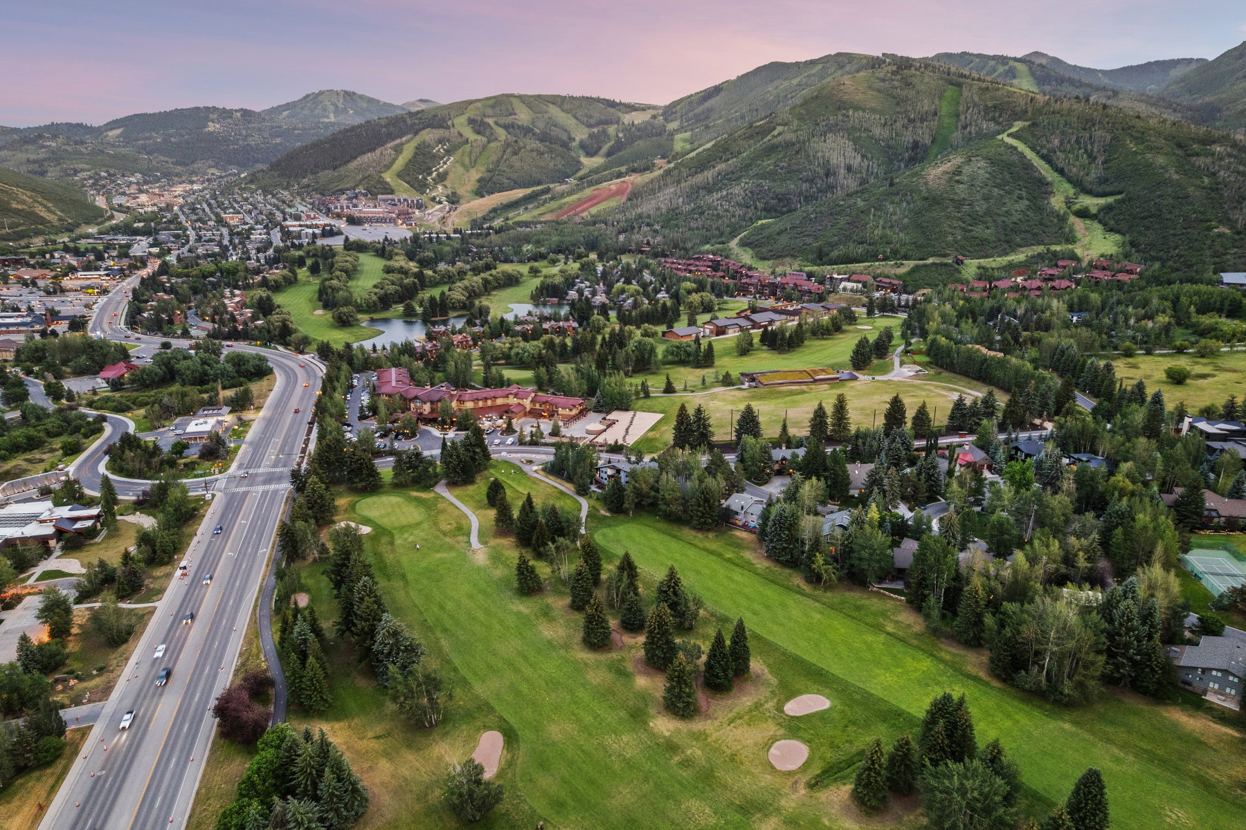 Aerial perspective showcasing a sprawling golf course, verdant mountain backdrop, and a substantial road network