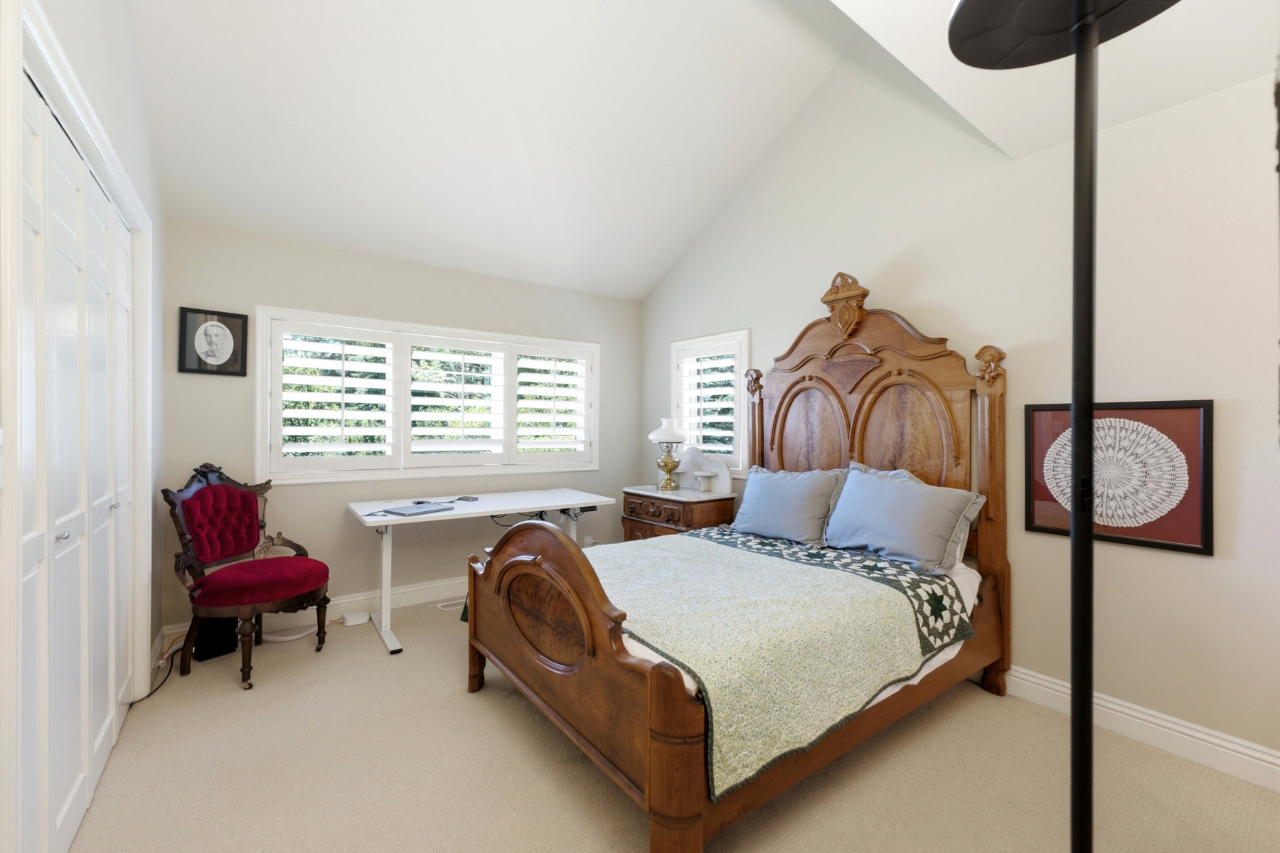 Vaulted ceiling room featuring a triple window with plantation shutters, cream-colored wall paint, and light-toned carpeting
