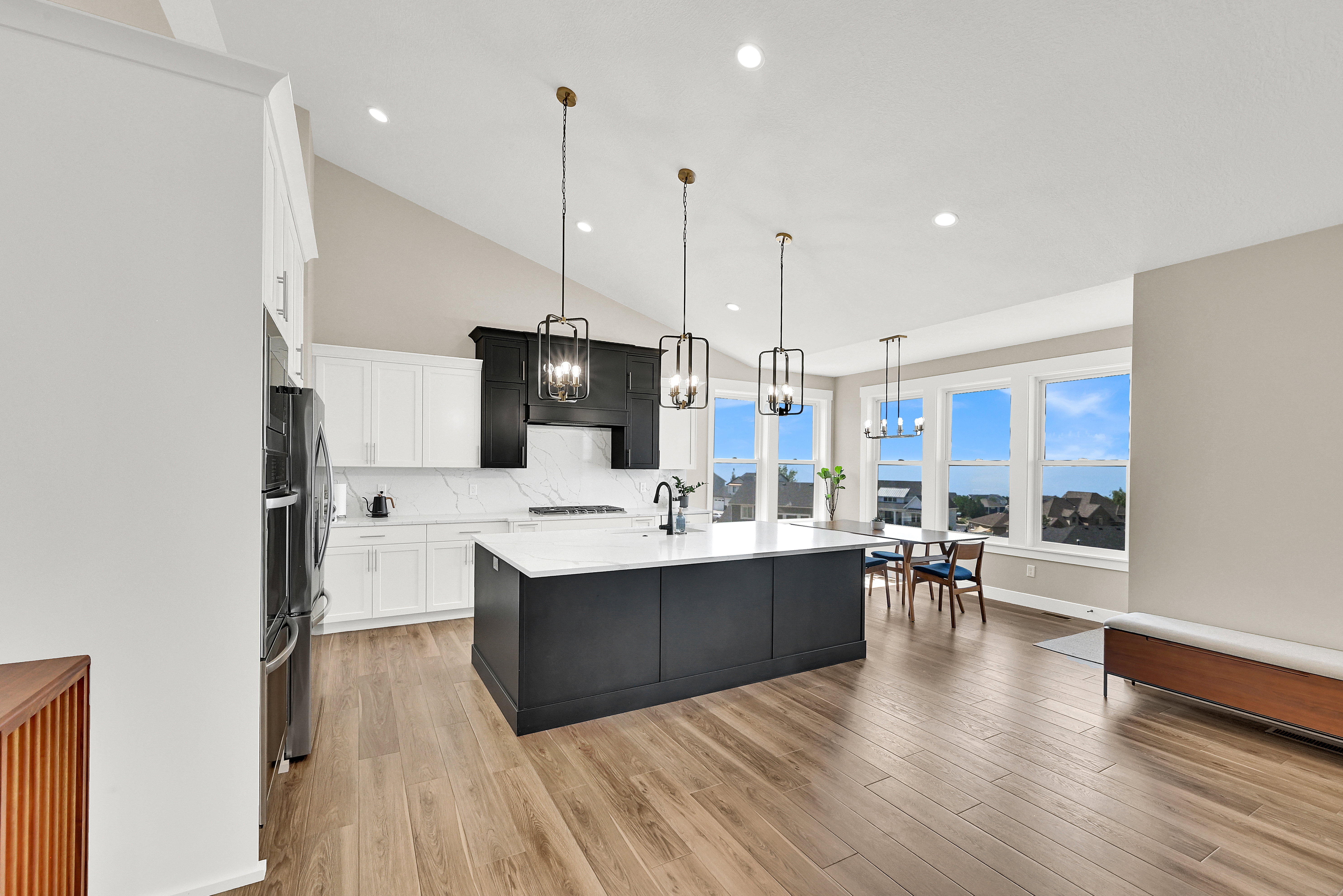 Spacious kitchen featuring an expansive island with a white countertop, two-tone cabinetry, wood-finish flooring, and a vaulted ceiling