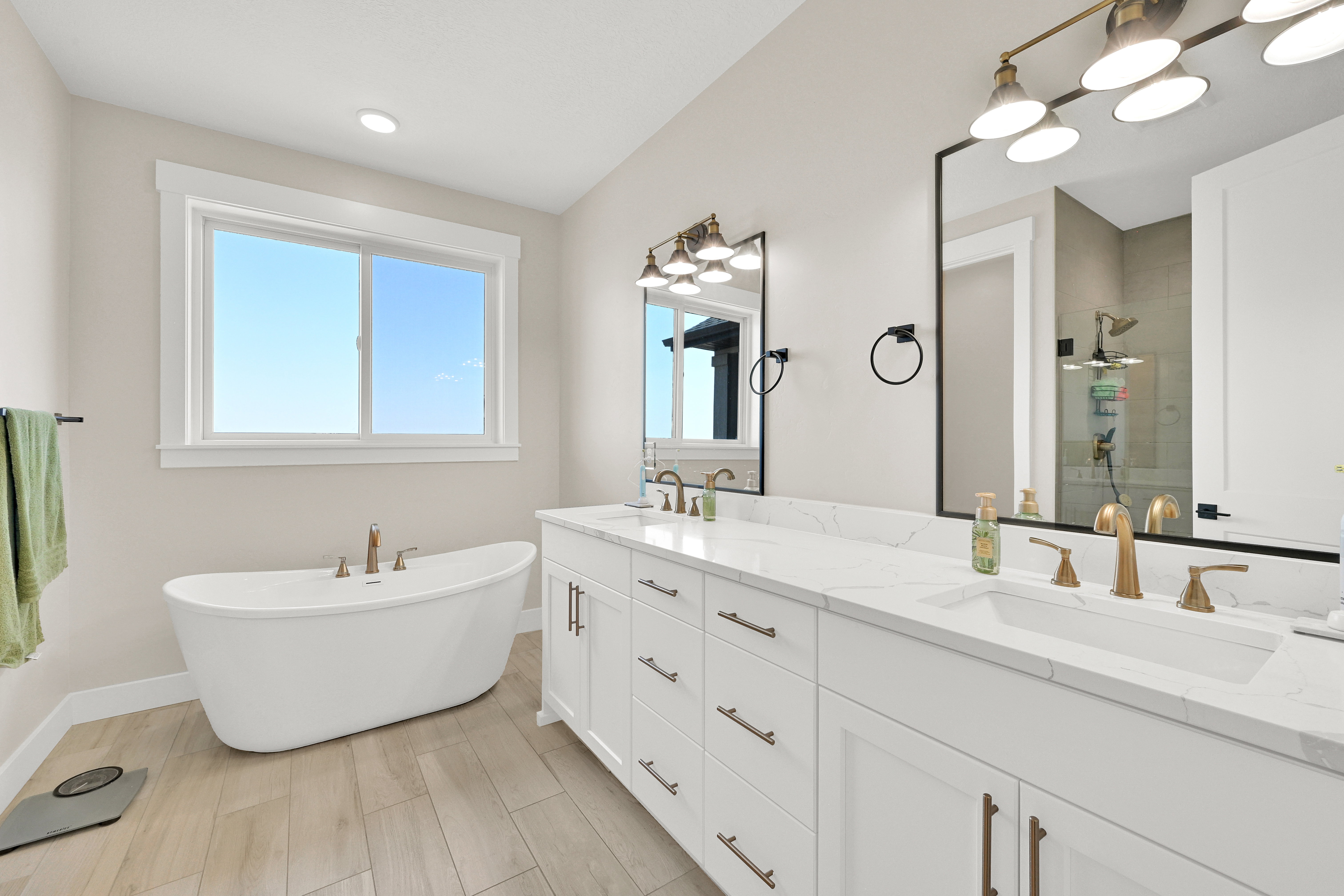 Spacious bathroom featuring a freestanding soaking tub, dual vanity with white cabinetry, quartz-finish countertops, and wood-finish flooring