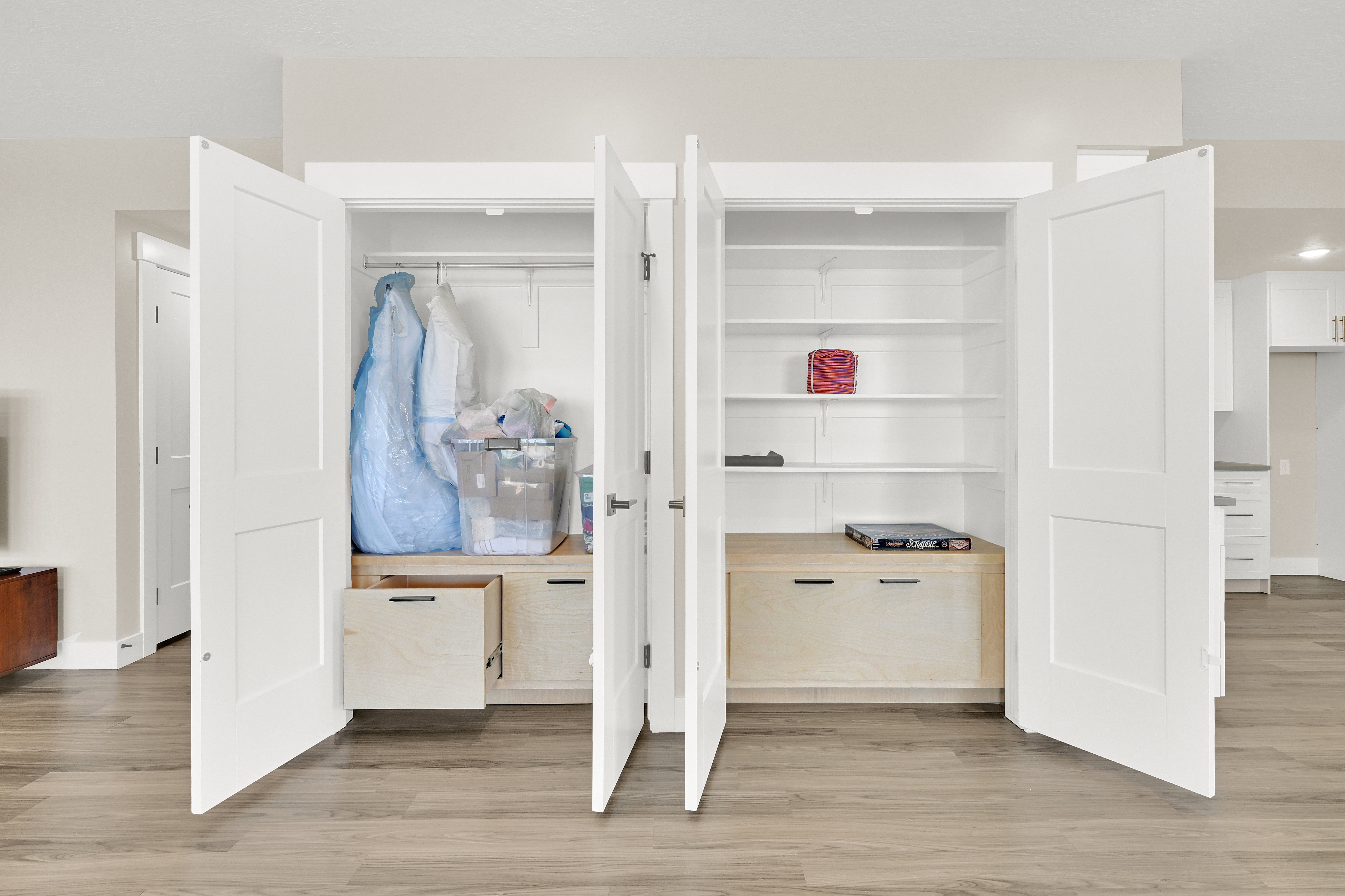 Built-in white storage closets featuring bi-fold doors, adjustable shelving, integrated wood-finish drawers, and hanging rods, all set against wood-finish flooring