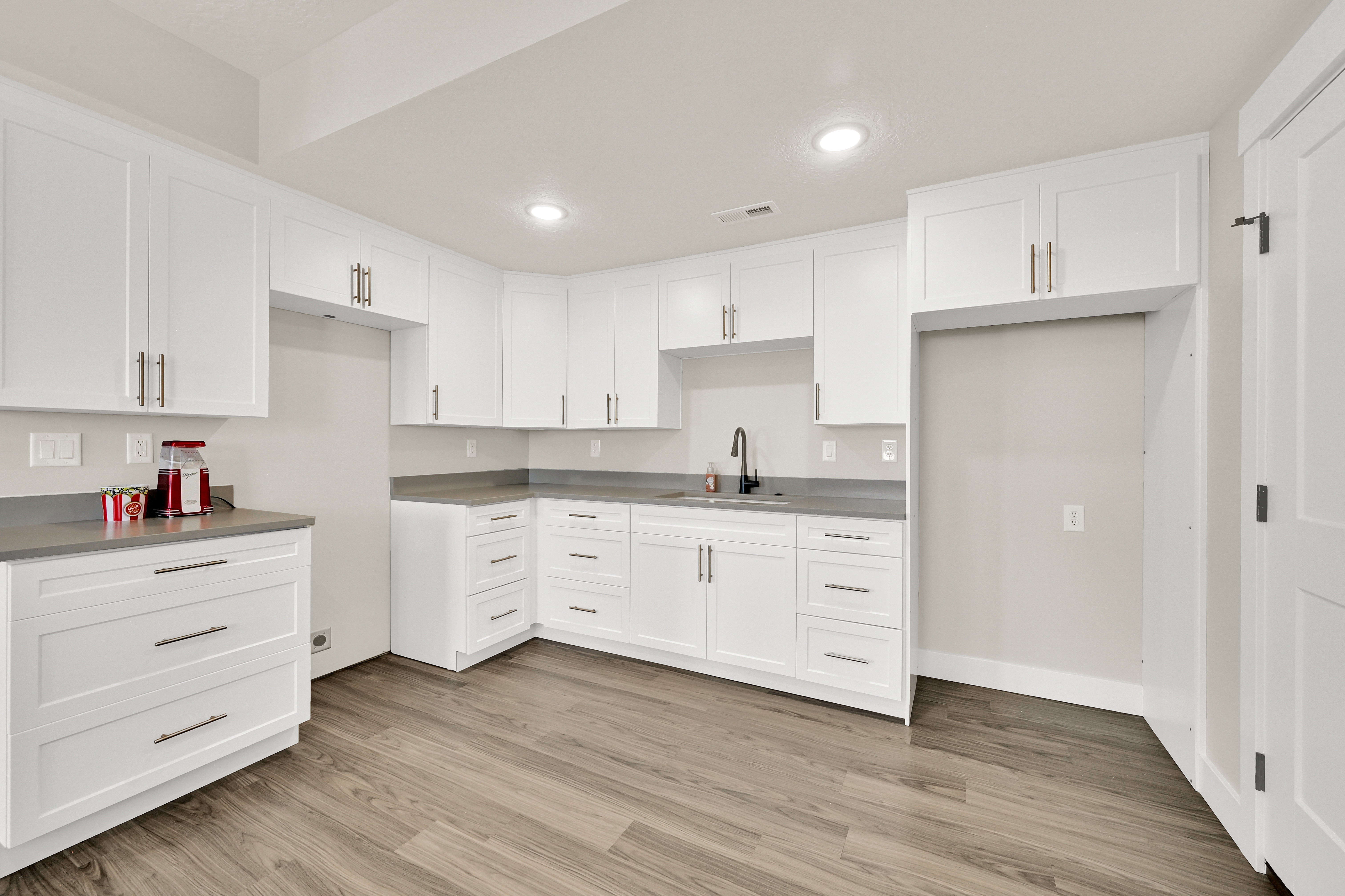 Kitchenette featuring white shaker-style cabinetry, dark wood-finish flooring, gray countertops, and a matte black gooseneck faucet