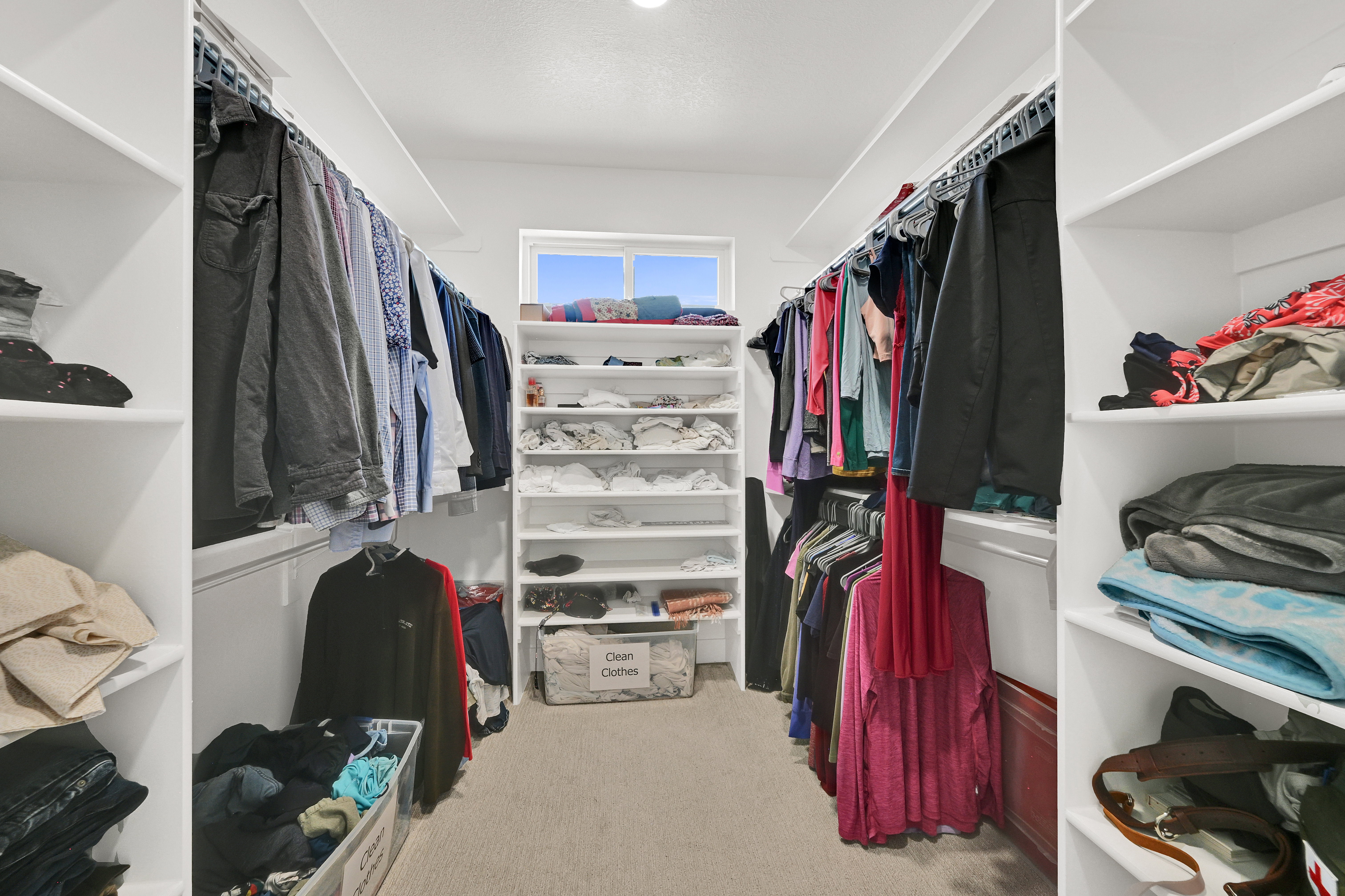Walk-in closet featuring built-in white shelving, multiple hanging rods, recessed lighting, and a window for natural light