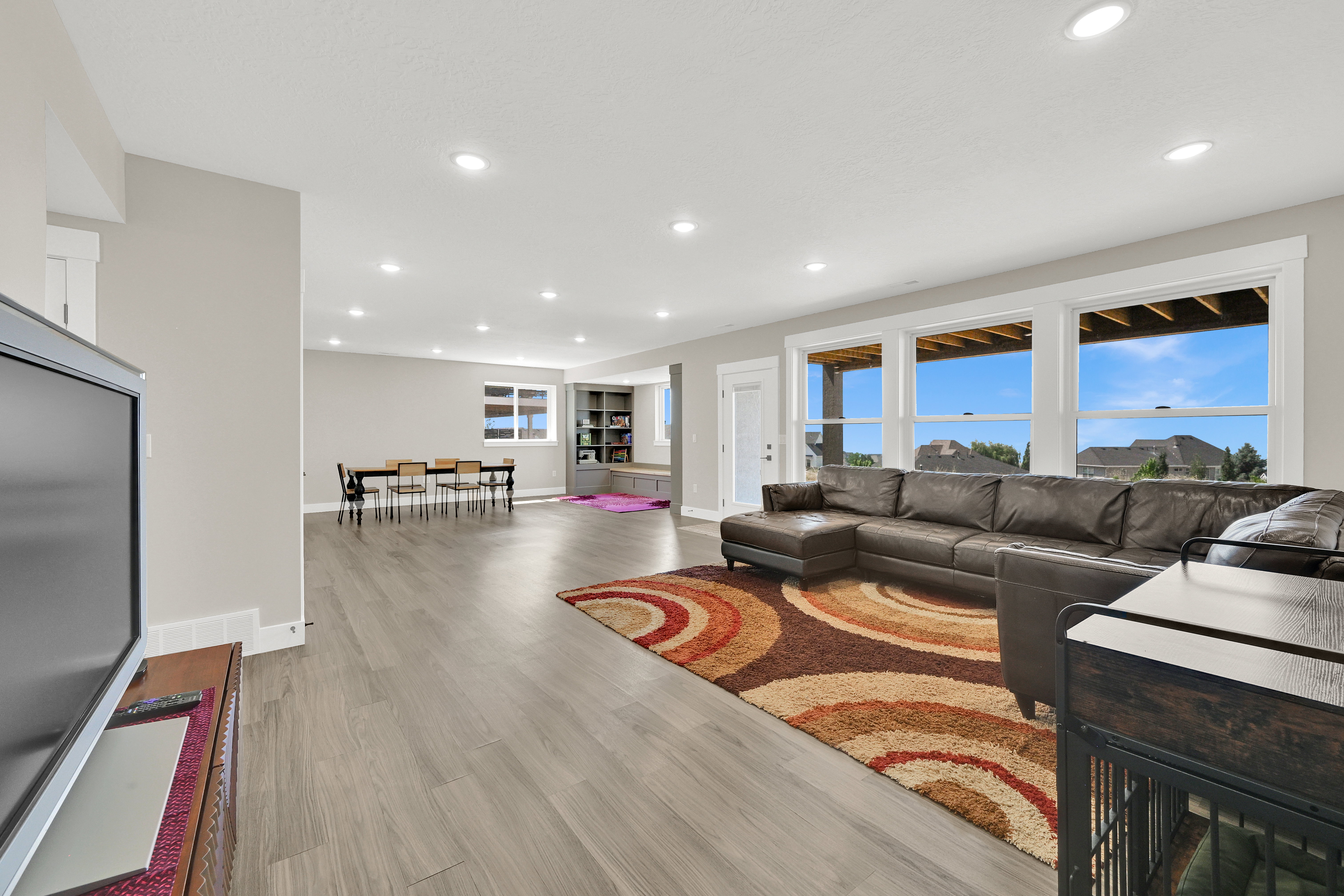 Spacious entertainment area featuring wood-finish flooring, recessed lighting, and large windows with white trim
