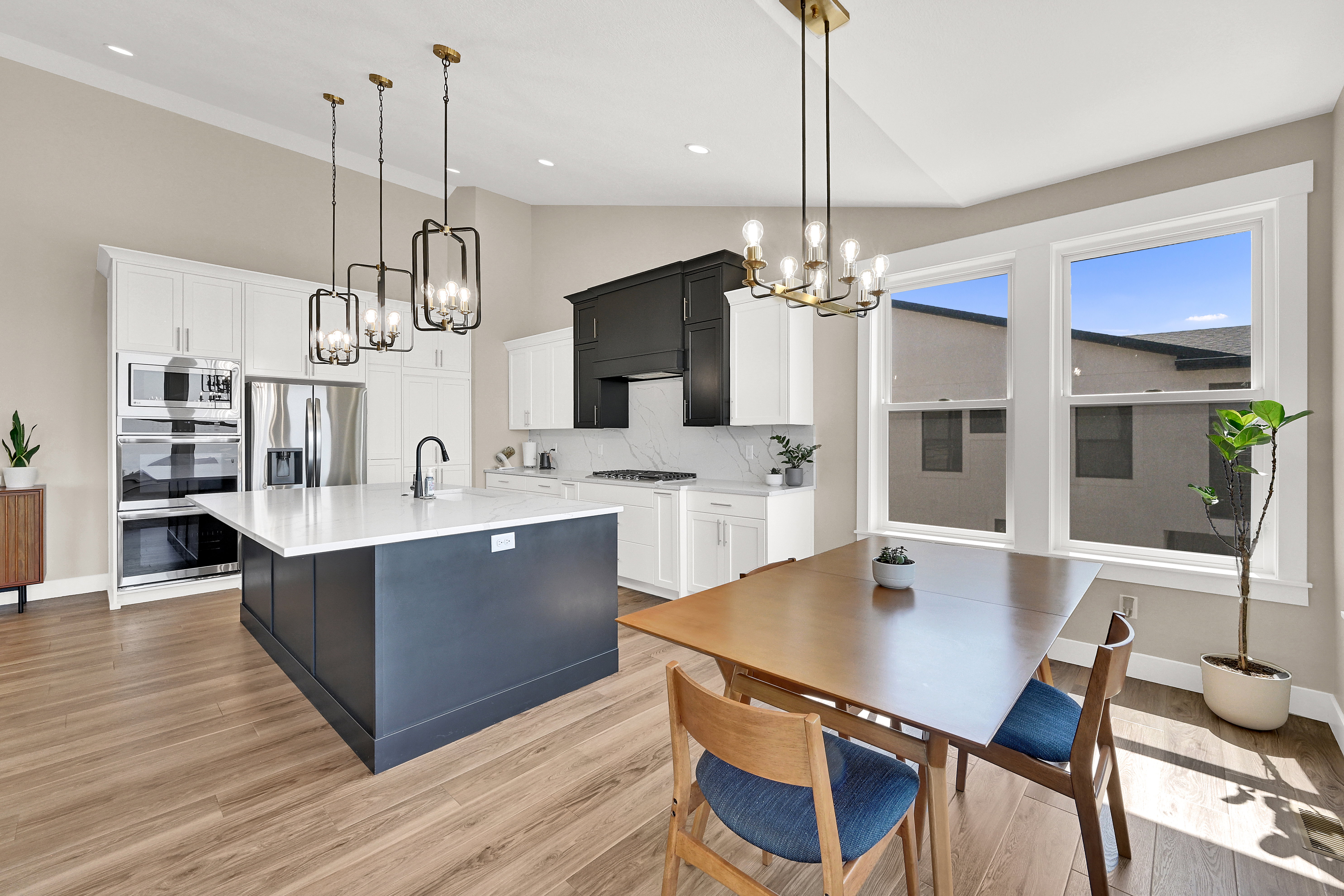 Open-concept kitchen and dining area featuring a prominent dark blue kitchen island with a white countertop, coordinating white upper and lower cabinetry, and a black range hood
