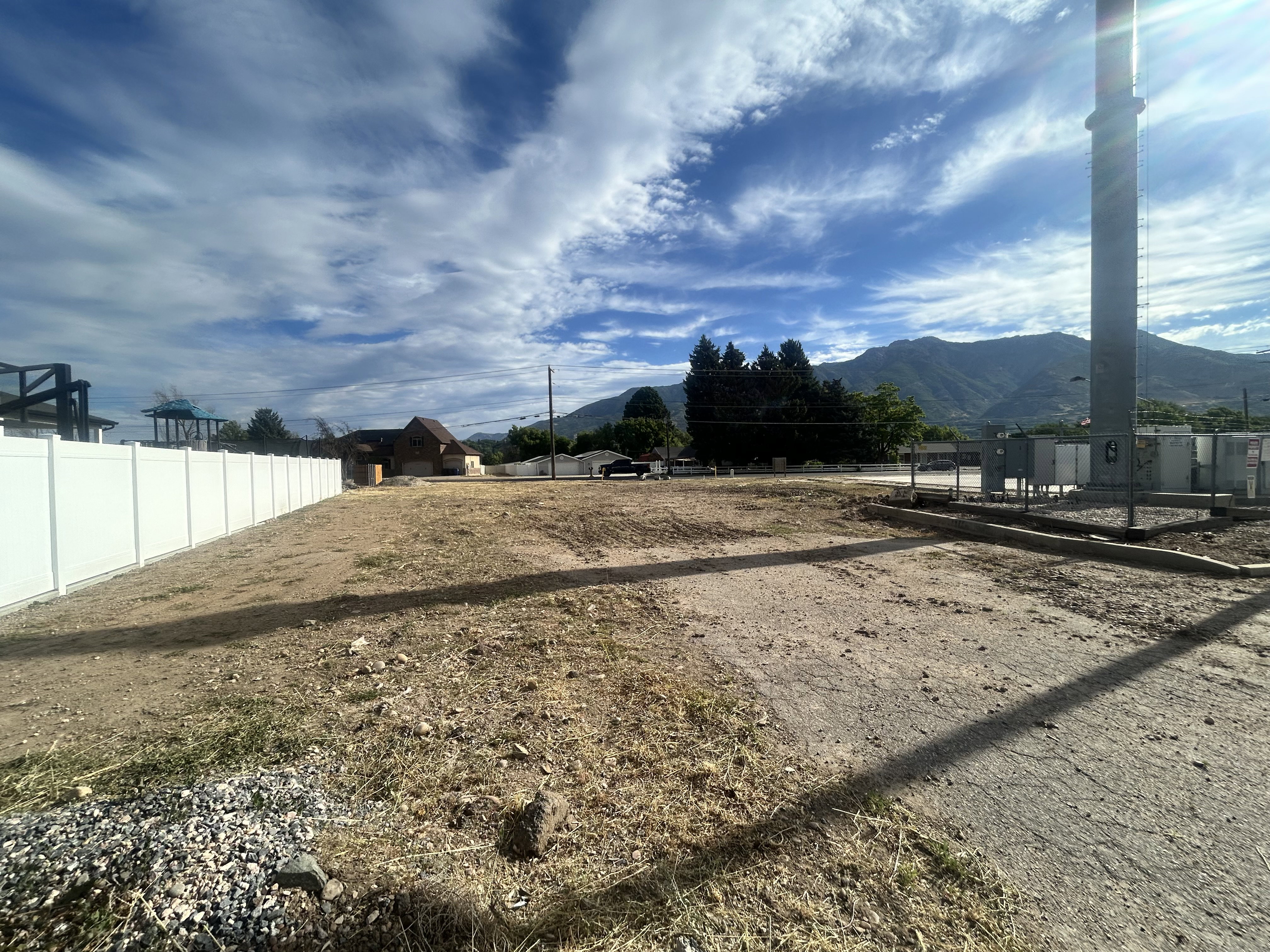 Level building lot featuring a white privacy fence, mountain backdrop, and utility infrastructure