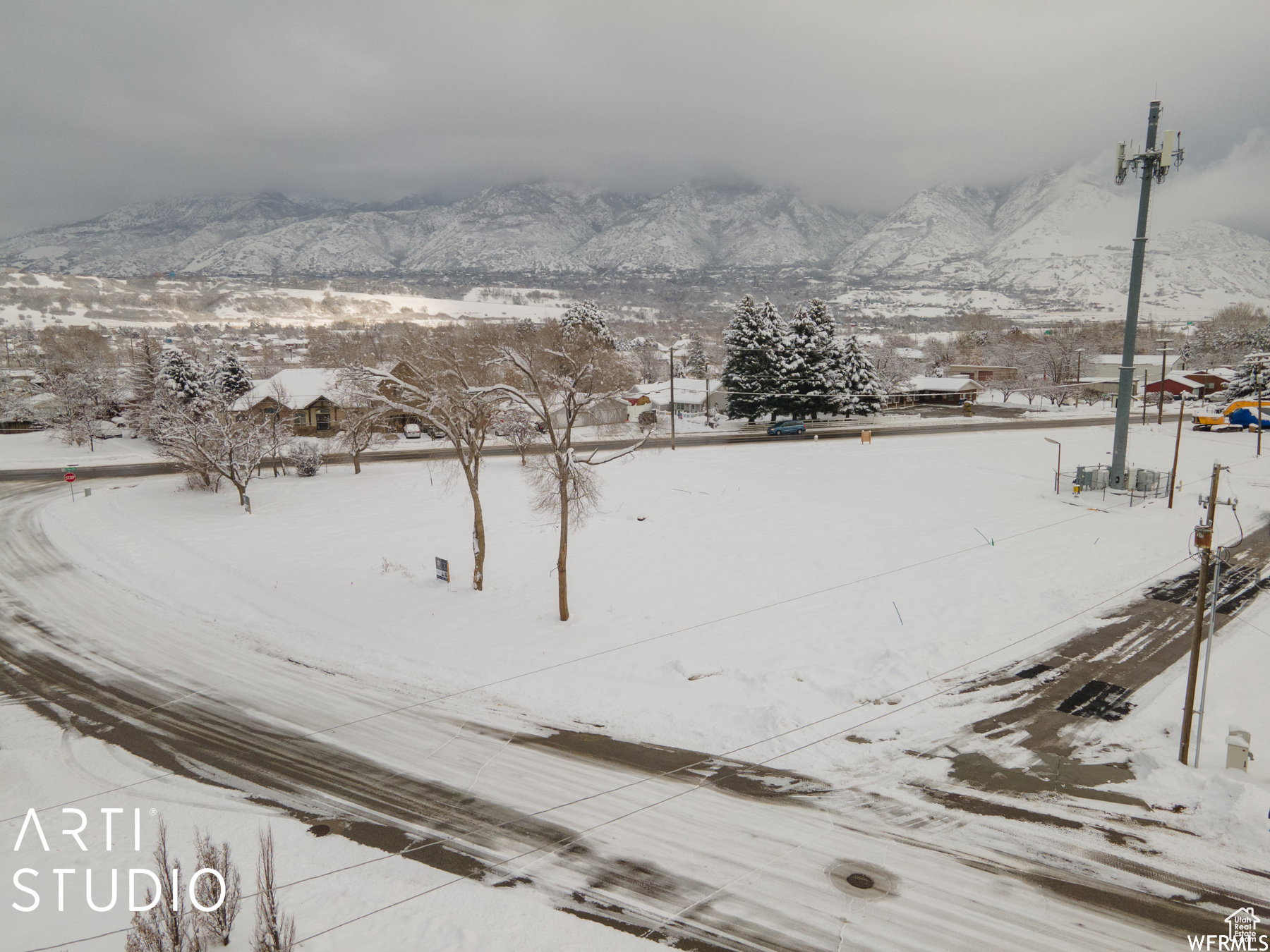 Expansive snow-covered lot featuring a paved road frontage and distant mountain scenery