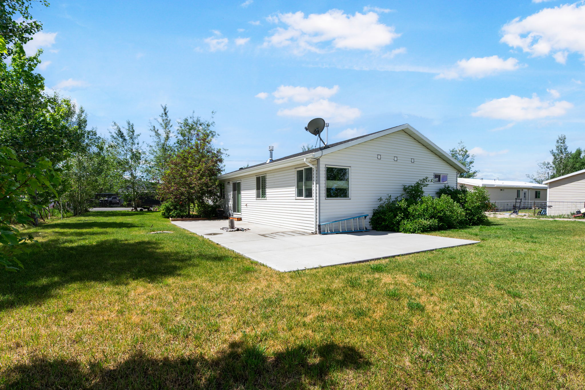 Spacious backyard featuring a large concrete patio, expansive lawn, mature trees, and white siding exterior