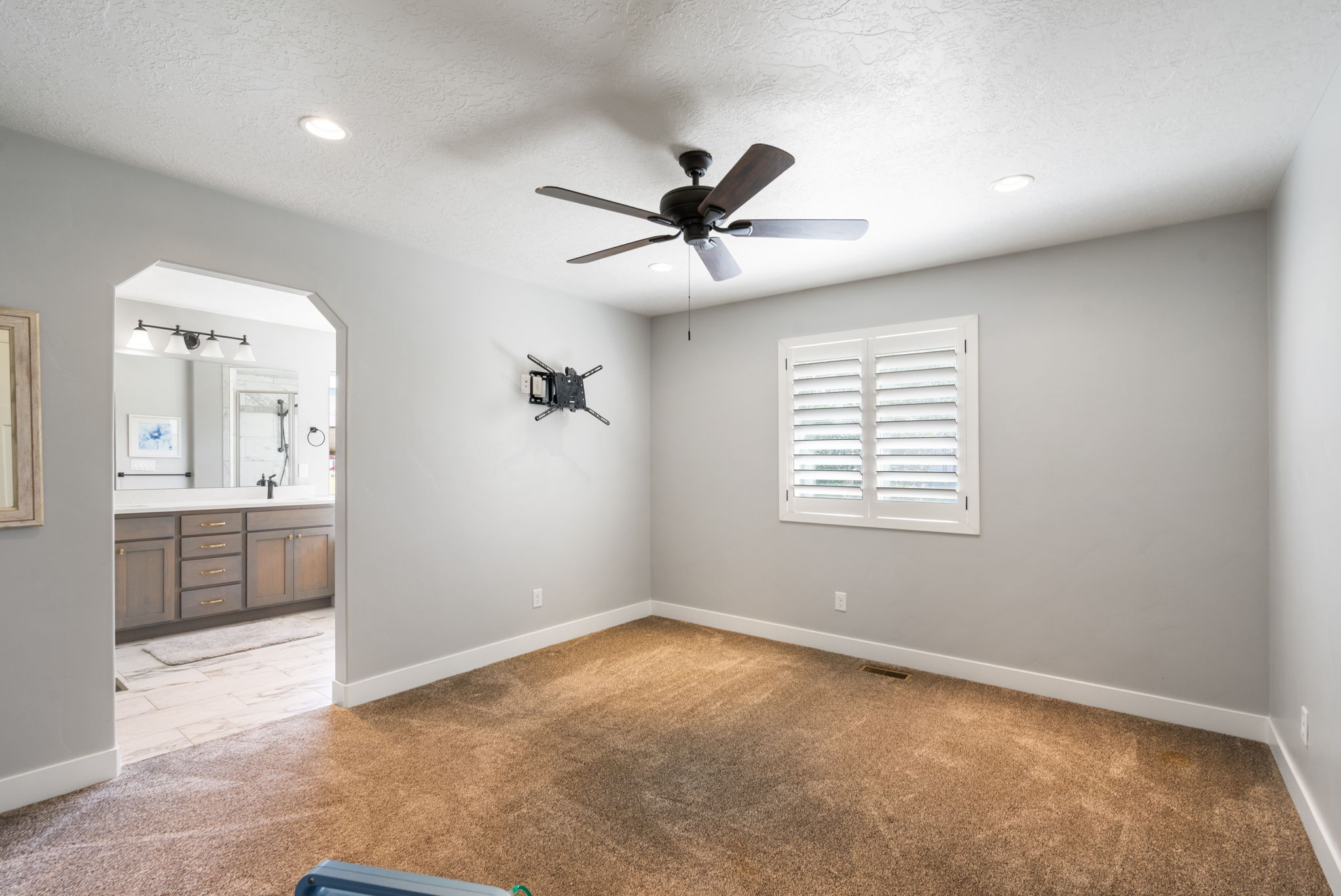 Carpeted bedroom featuring a ceiling fan with integrated lighting, recessed ceiling lights, and a window with white plantation shutters