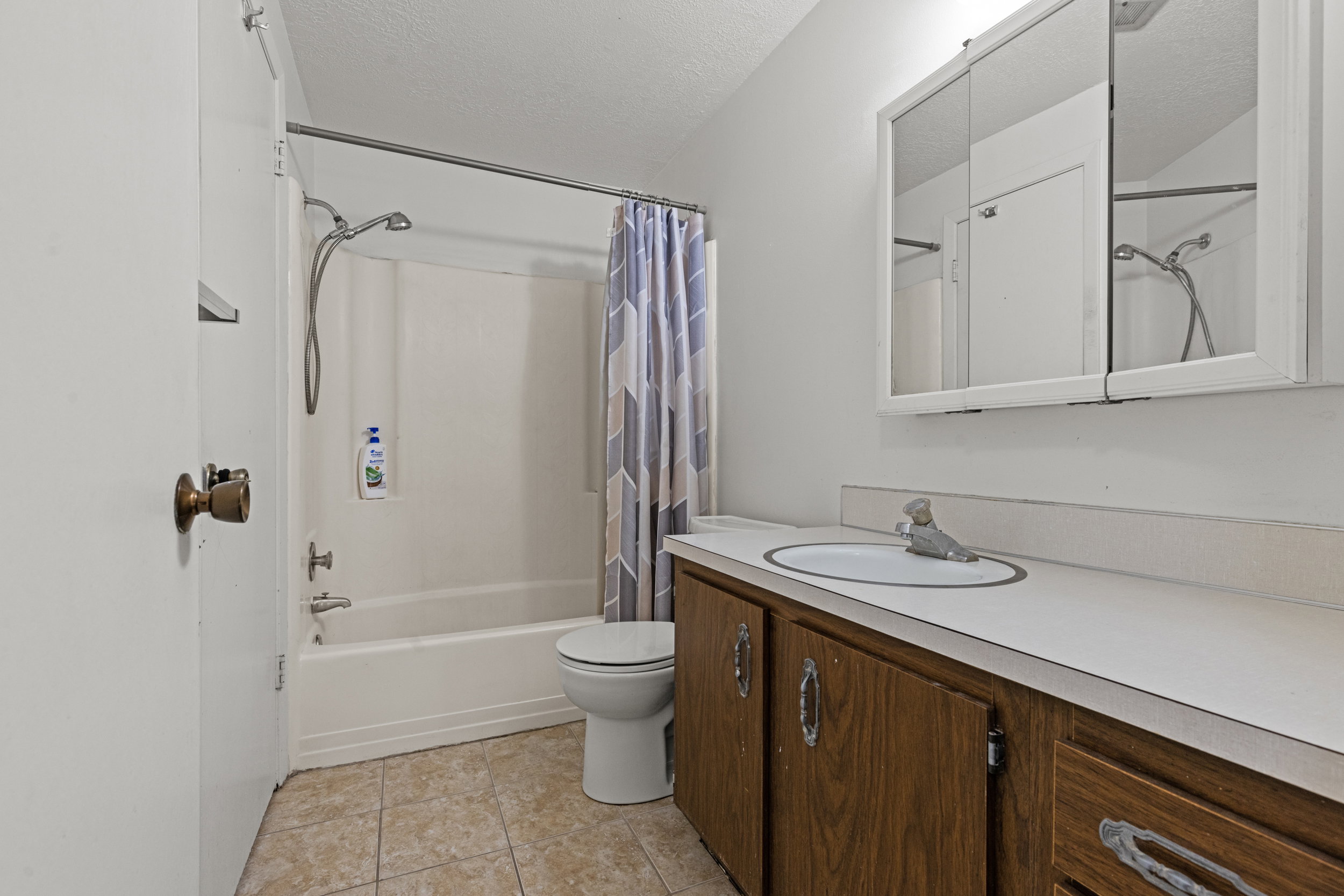Full bathroom featuring a white tub/shower combination, white toilet, and a vanity with a white countertop and wood-finish cabinetry