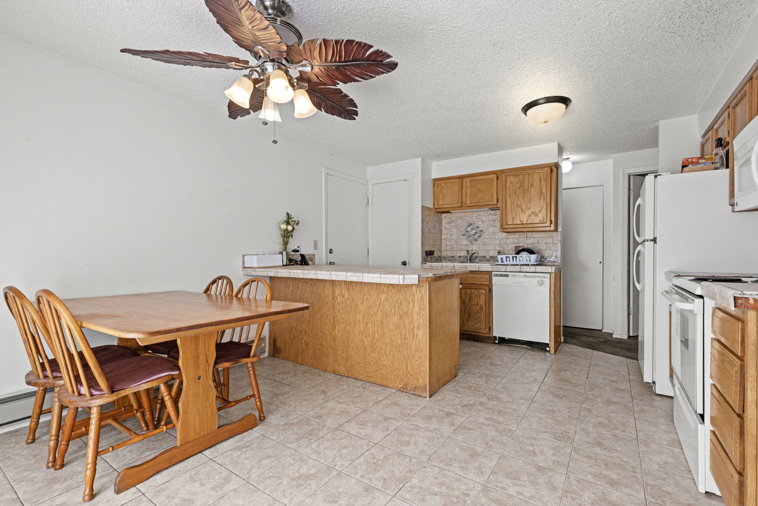 Open-concept kitchen and dining area featuring tile flooring, wooden cabinetry, and white appliances