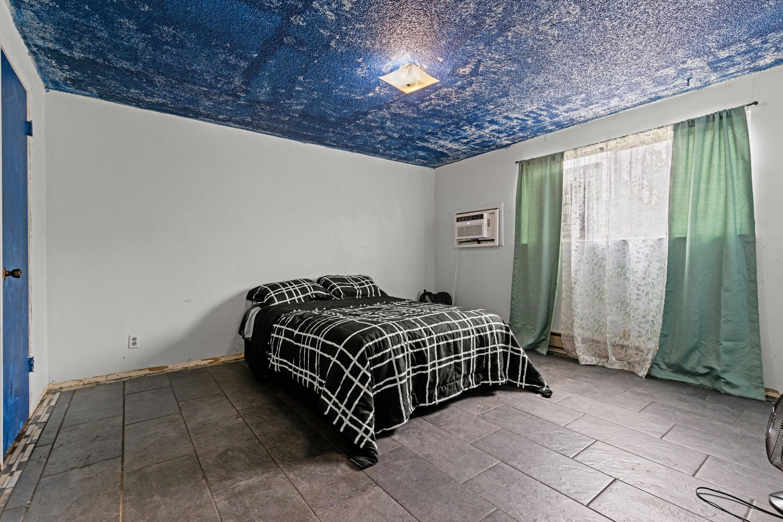 Rectangular floor tiles, light gray walls, and a window with green drapes