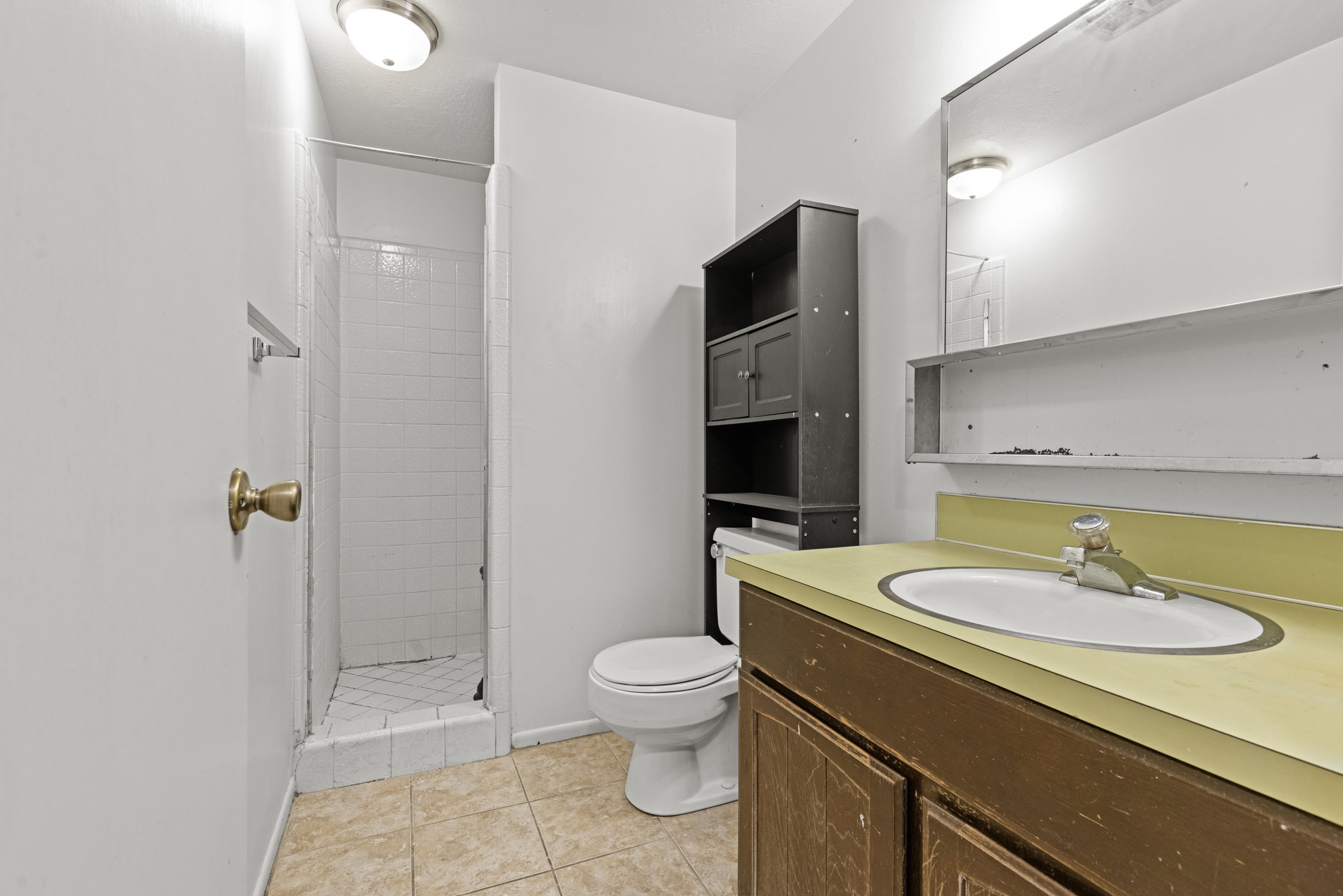 Bathroom featuring a standing shower with white tile surround, ceramic tile flooring, a white toilet, and a vanity with an integrated sink and yellow countertop