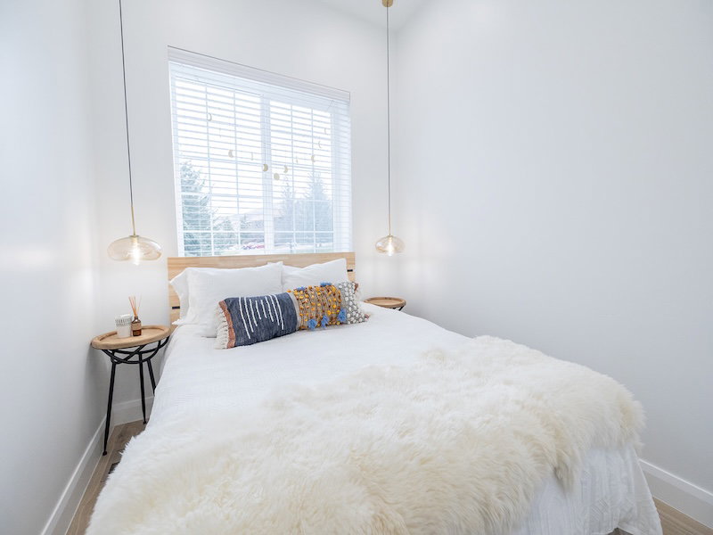 Light-filled room featuring a large window with blinds, wood-finish flooring, and crisp white walls