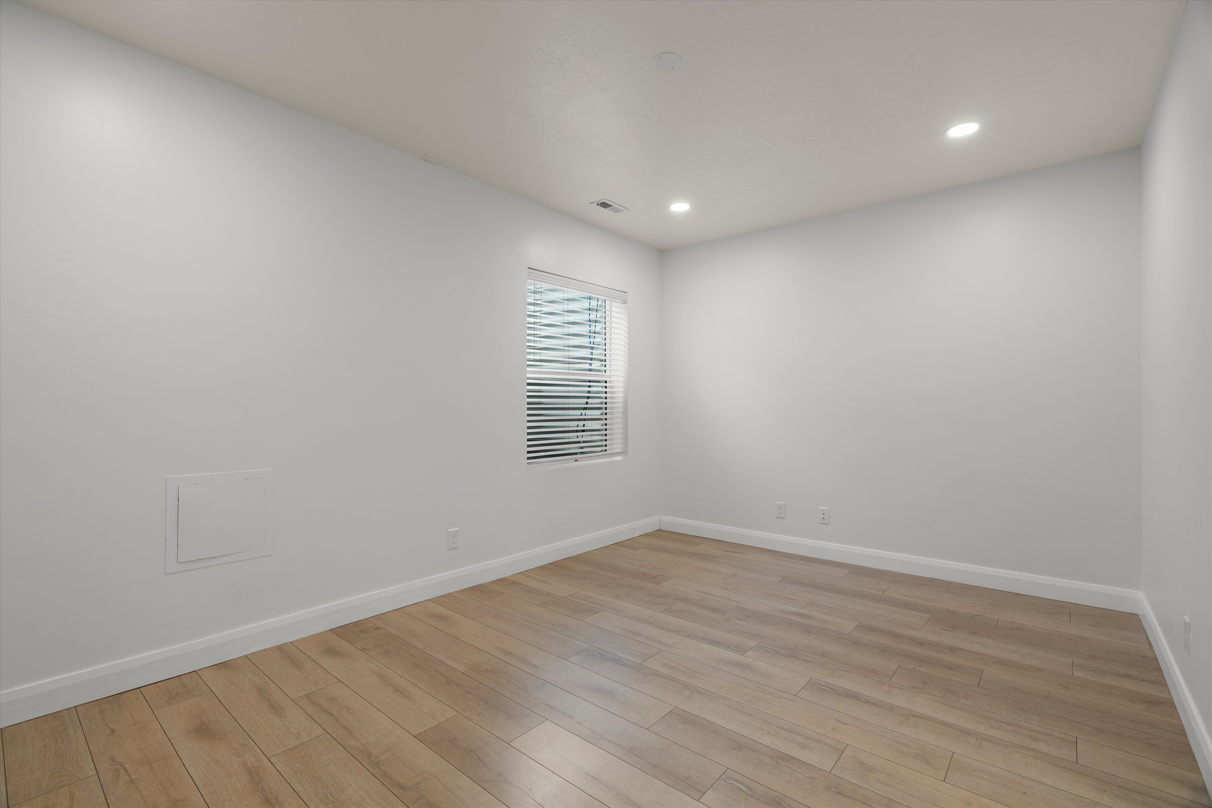 Spacious room featuring light wood-finish flooring, white baseboards, and neutral wall paint