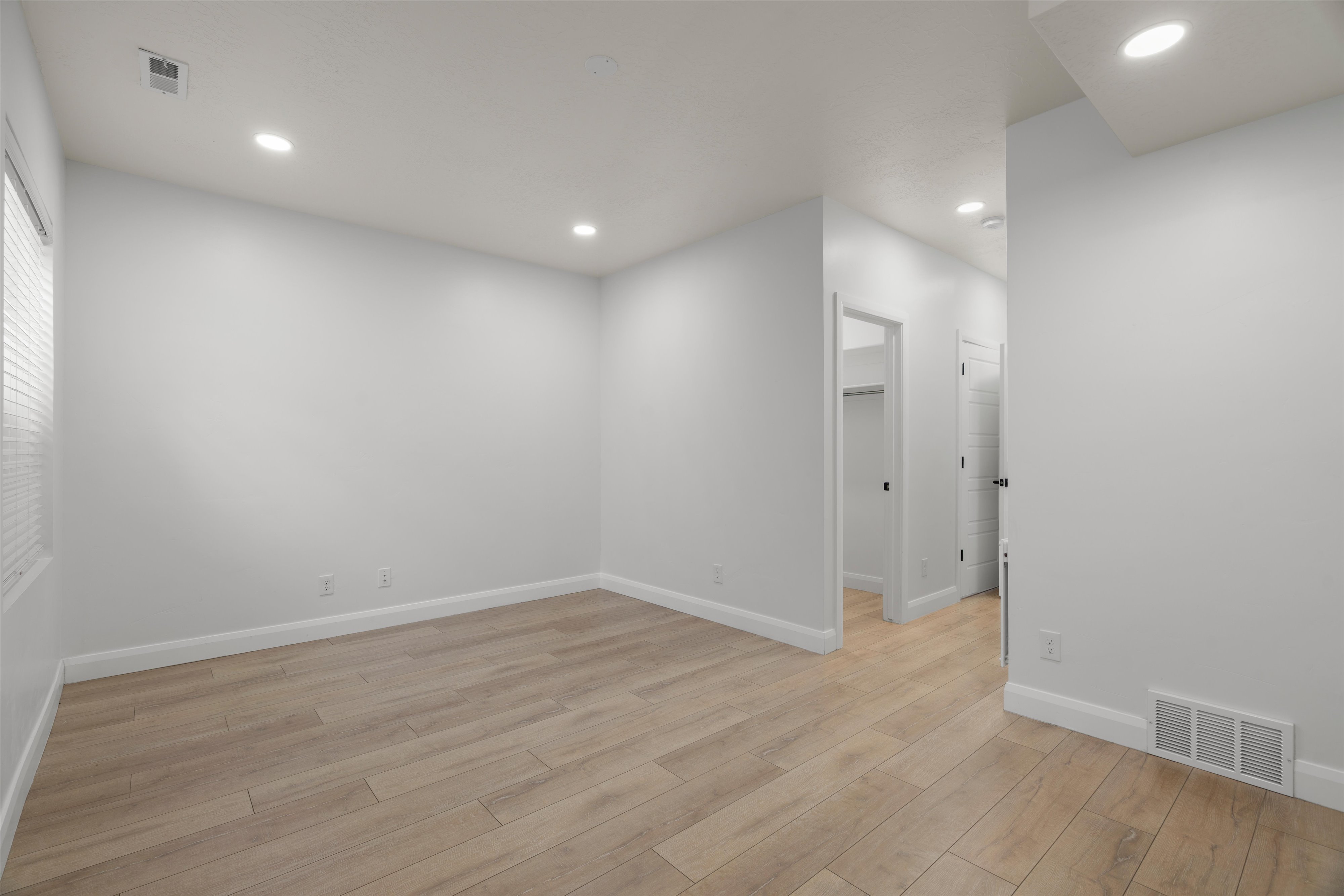 Spacious room featuring light wood-finish flooring, recessed lighting, neutral wall tones, and white baseboards