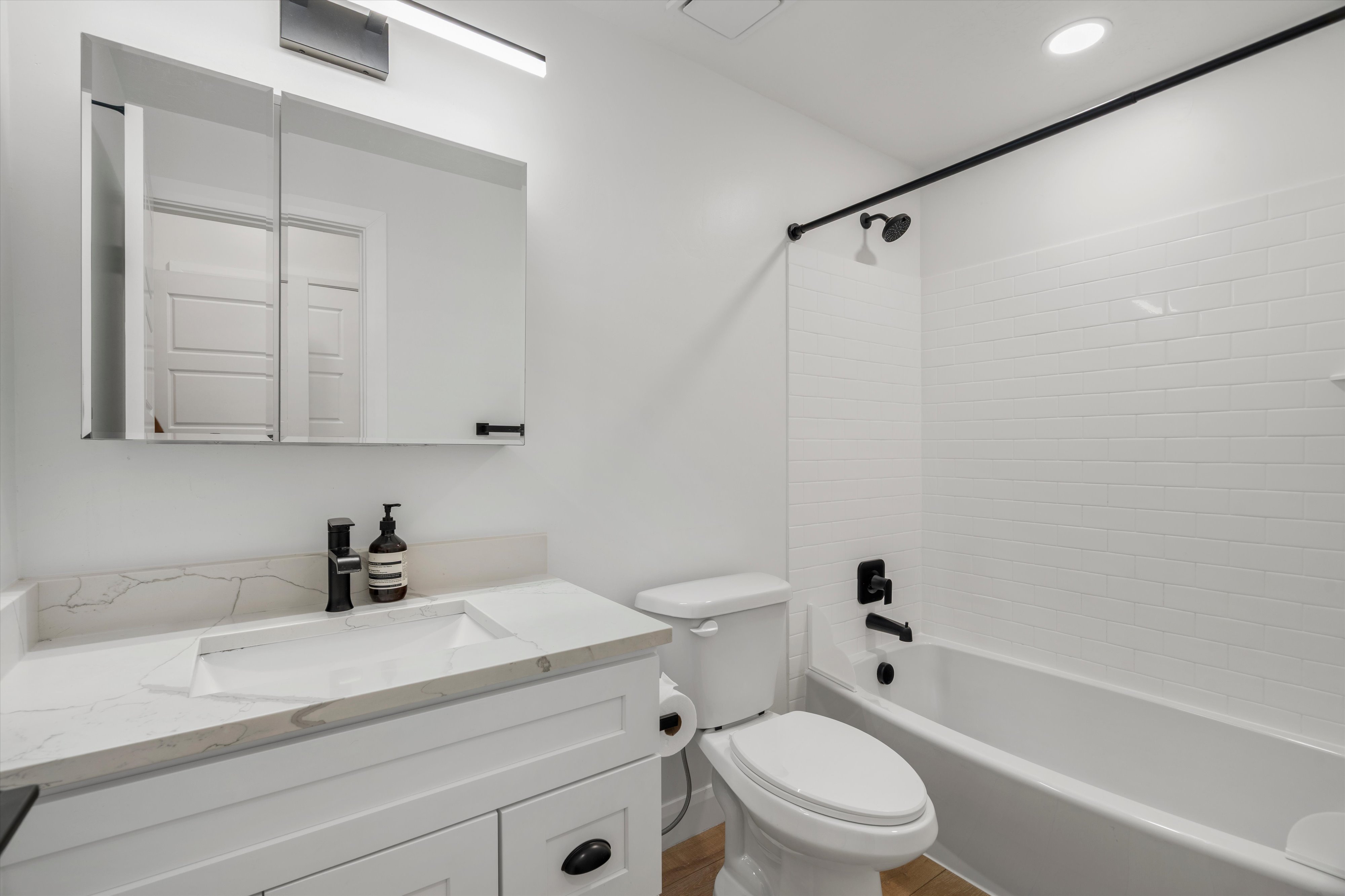 Bathroom featuring a white vanity with a light-toned countertop and integrated sink, matte black faucet, and mirrored medicine cabinet