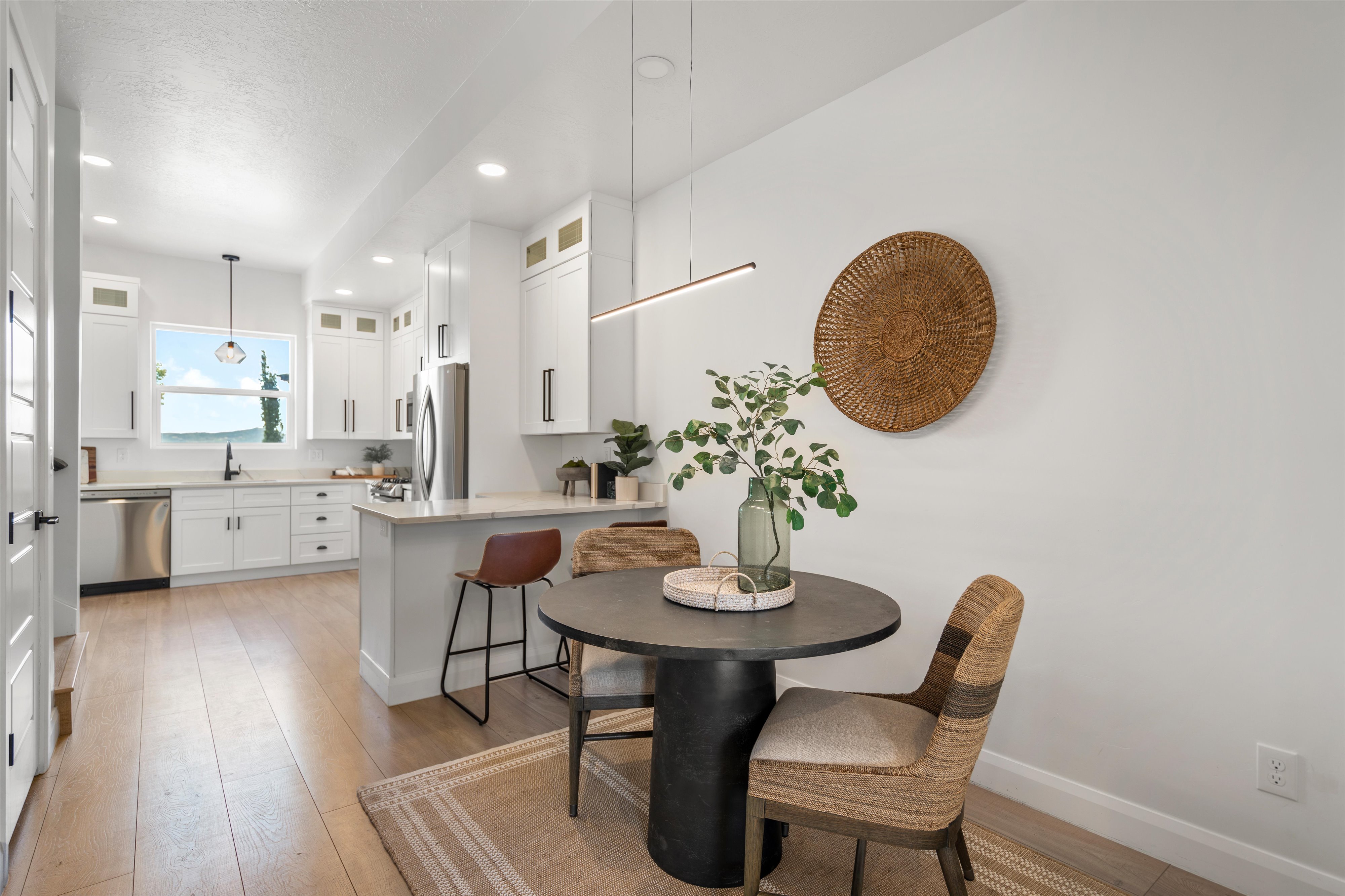 Contemporary kitchen with white cabinetry, light wood-finish flooring, stainless steel appliances, a breakfast bar, and a window with a scenic backdrop