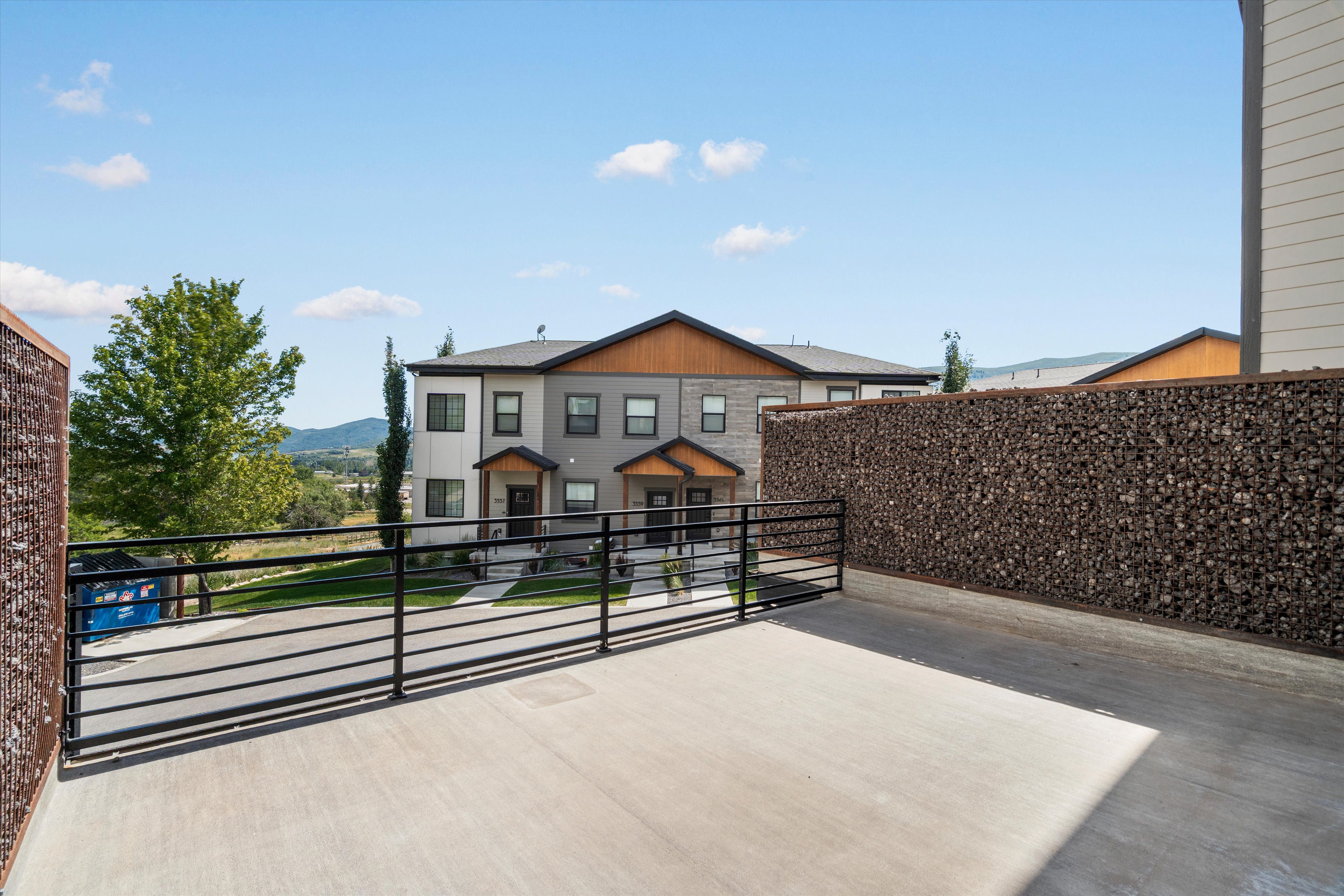Spacious concrete patio featuring black metal railings and gabion walls